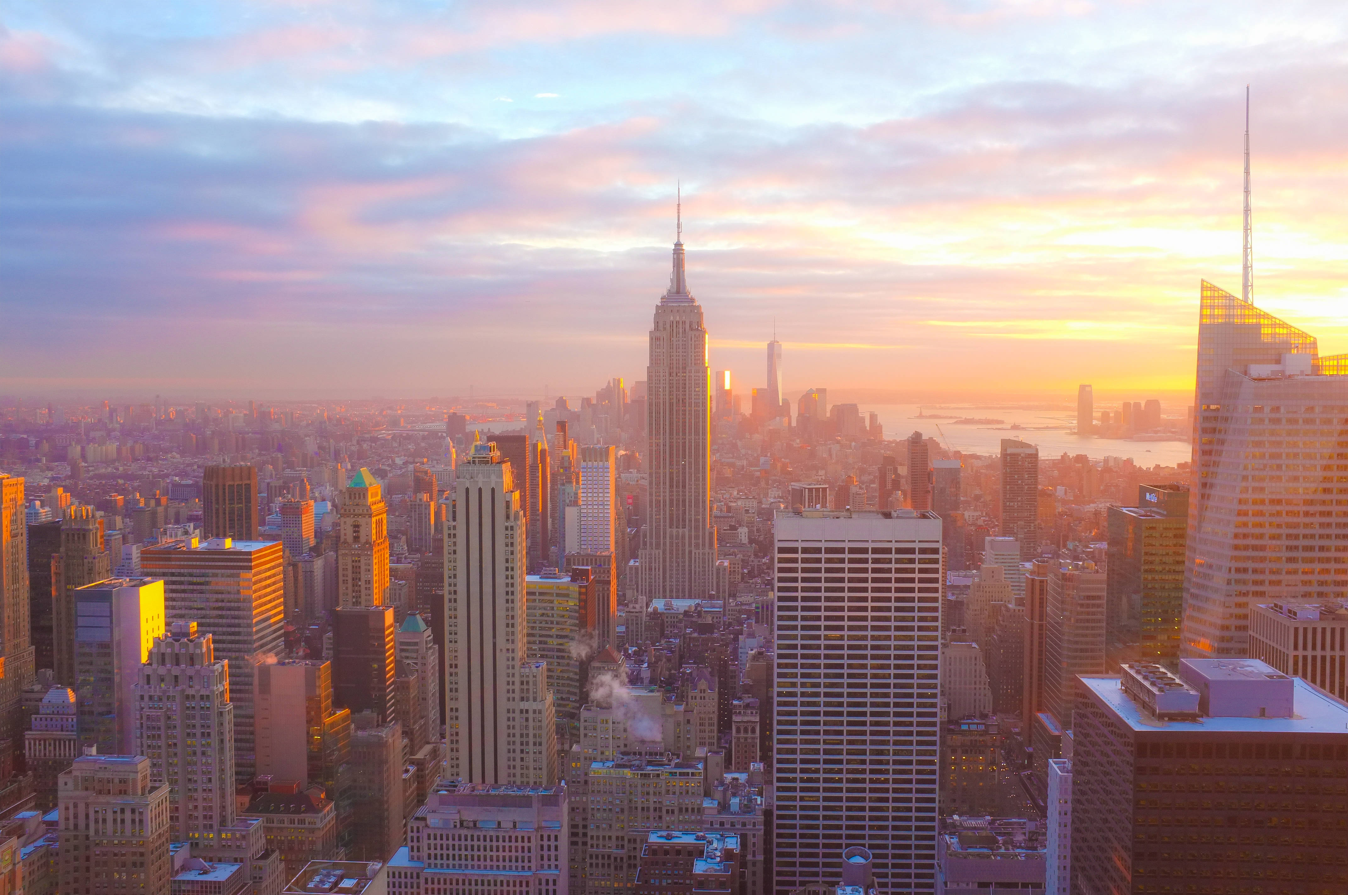 Skyscraper 桌布 壁紙 — 令人嘆為觀止的日出將紐約市天際線沐浴在溫暖的金色光芒中，帝國大廈聳立在密集的城市景觀之上。