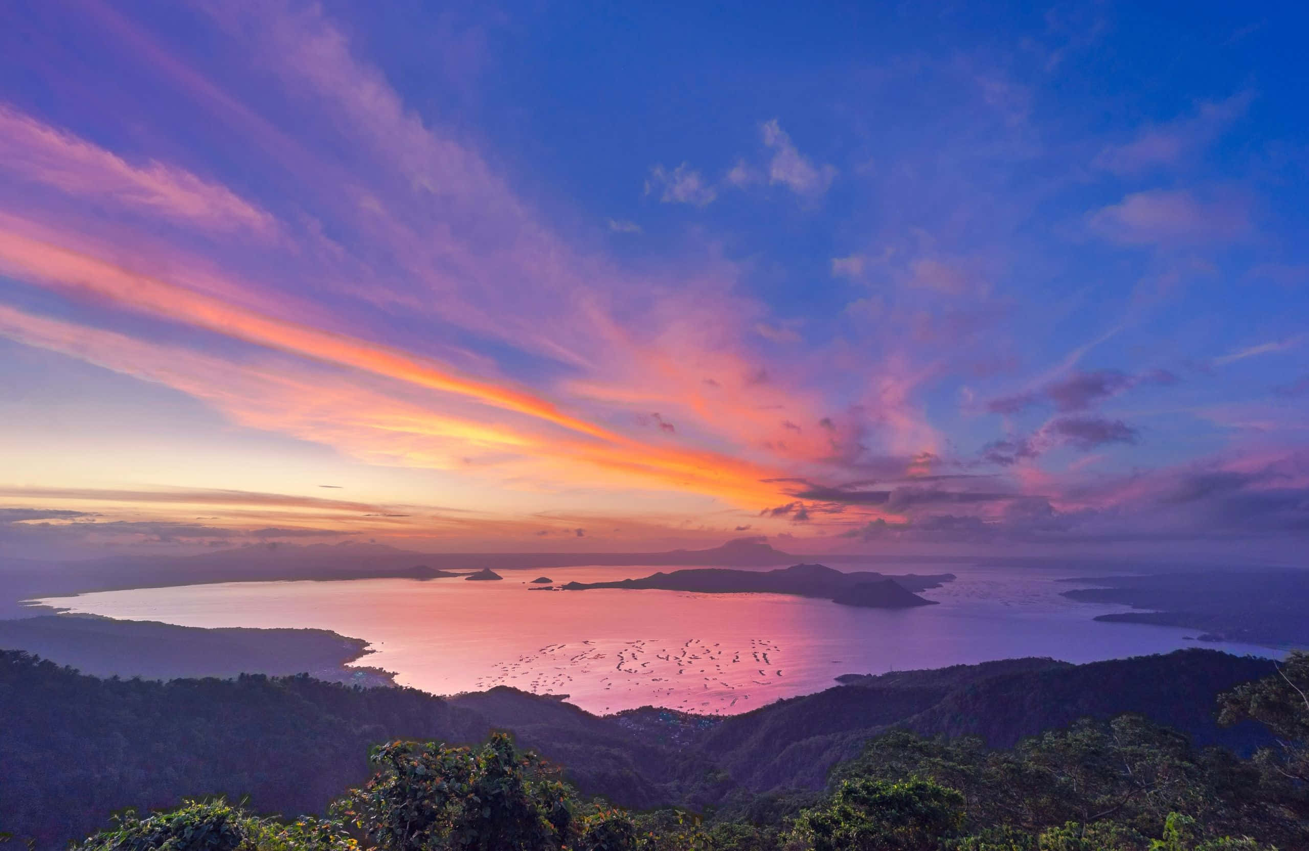 2560x1664 桌布 壁紙 — 令人嘆為觀止的日落，在寧靜的海灣上空，被鬱鬱蔥蔥的綠色山丘環繞，將天空染成火熱的橙色和紫色。