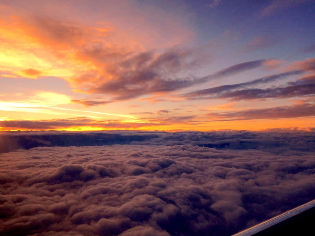 Airplane Window 桌布 壁紙 — 令人嘆為觀止的日落，從蓬鬆雲海之上，將天空染成火熱的橙色和紫色。