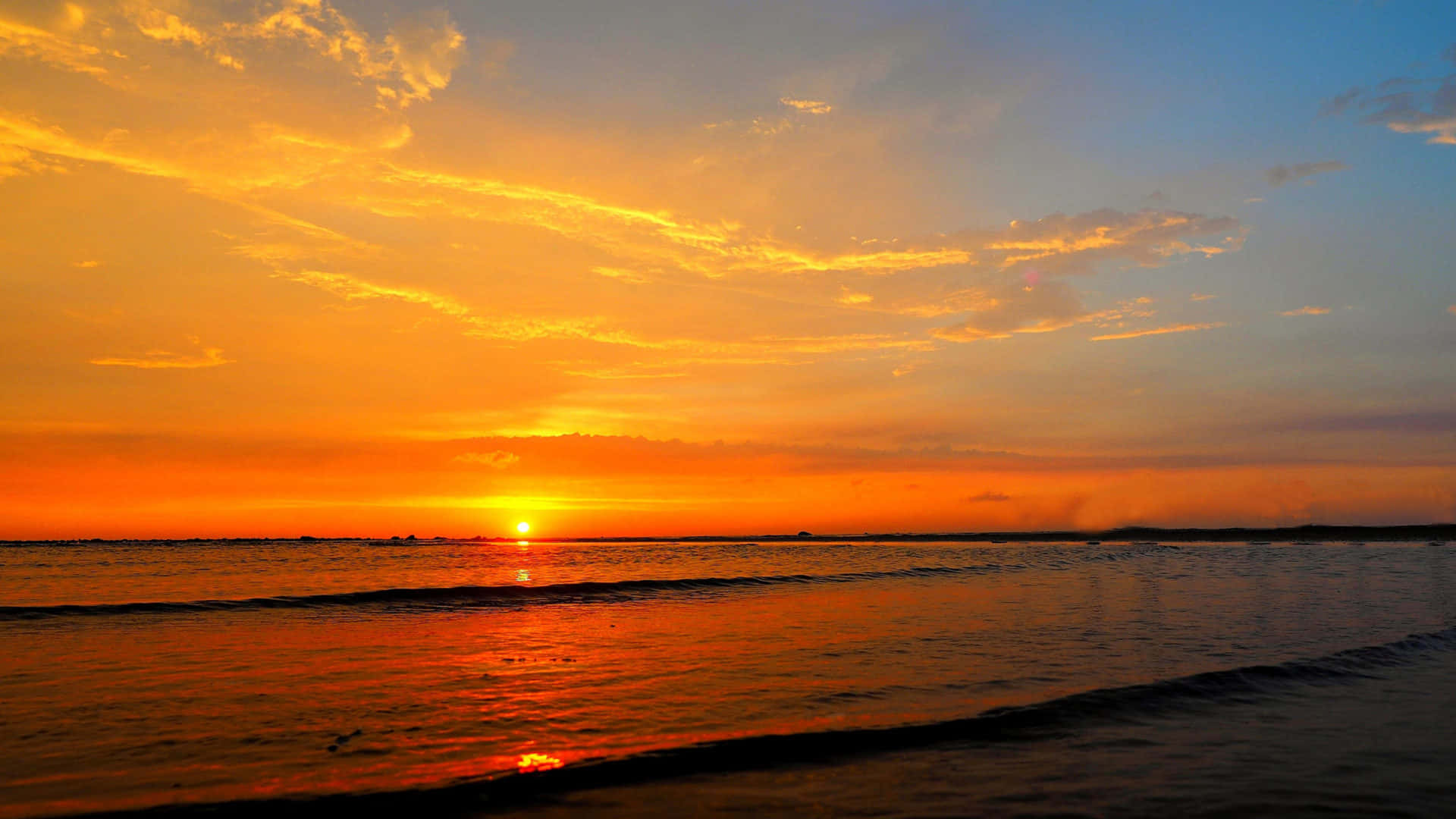 Sunset Ocean 桌布 壁紙 — 令人嘆為觀止的日落，映照在平靜的海面上，火紅的橙雲與金色的夕陽在溫柔的波浪上閃爍。