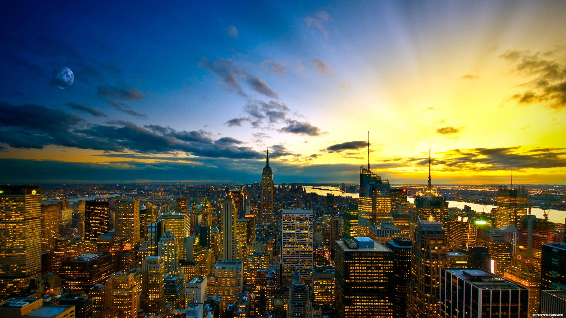 New York Skyline 桌布 壁紙 — 令人嘆為觀止的日落，照耀著密集的城市天際線，金色光芒穿透雲層，暮色天空中可見月亮。