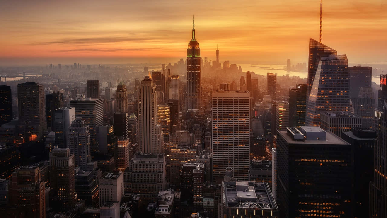 720p Ny City 桌布 壁紙 — 令人嘆為觀止的日落，金色光芒照亮紐約市天際線的摩天大樓和閃爍的窗戶。