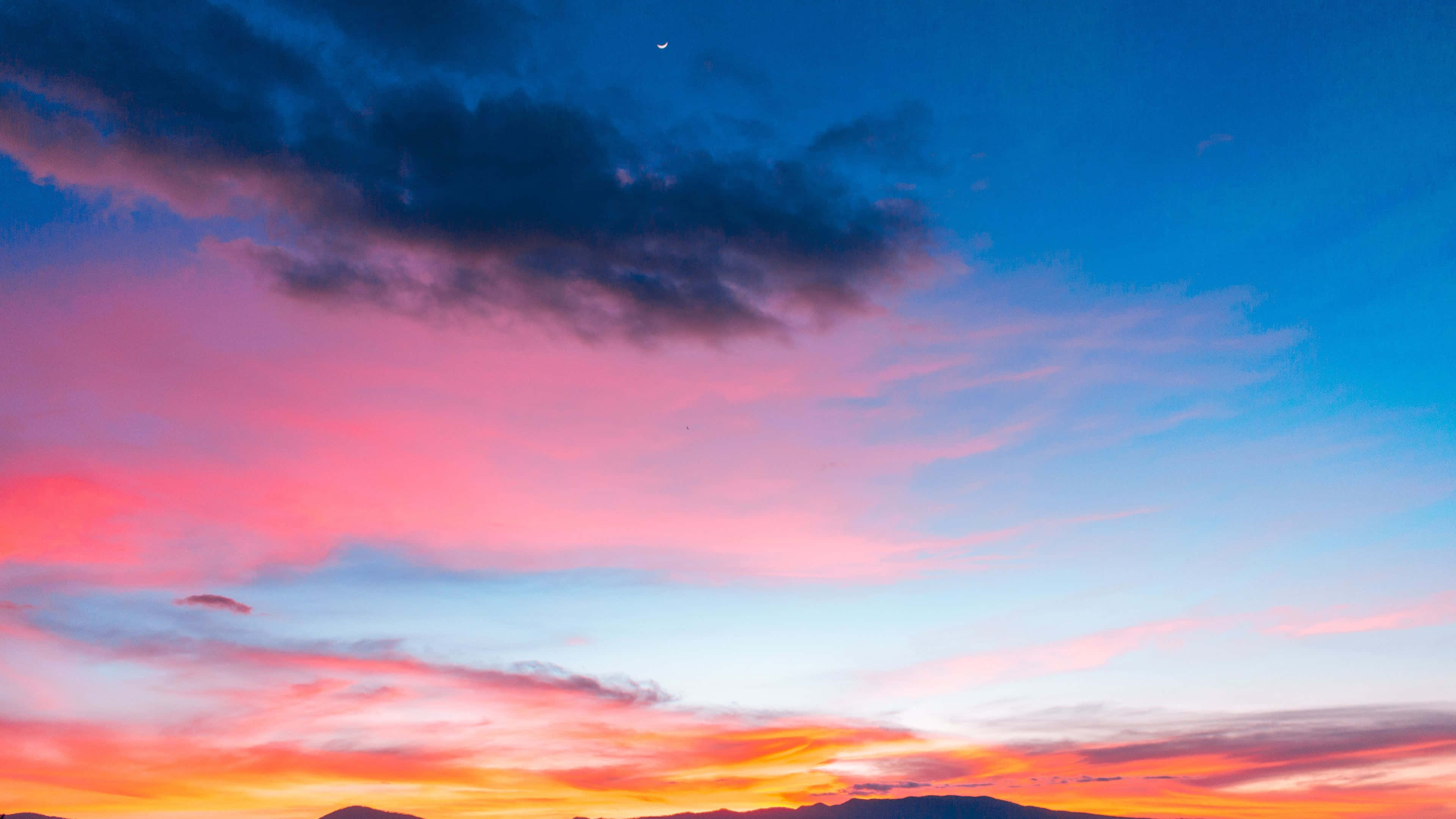 Colorful Sky 桌布 壁紙 — 令人嘆為觀止的日落天空，以火熱的橙色、粉紅色和深藍色雲彩繪製，遠處山巒輪廓之上。