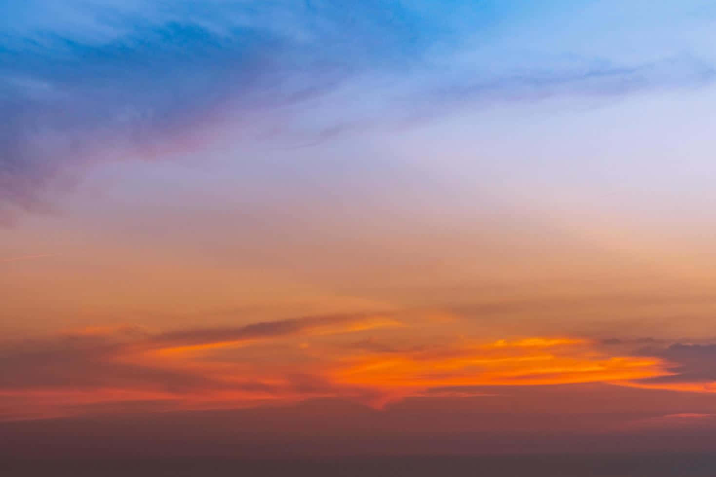 夕陽天空 桌布 壁紙 — 令人嘆為觀止的日落天空，火橙色的雲朵在遙遠的地平線上方融入柔和的藍色和紫色色調。