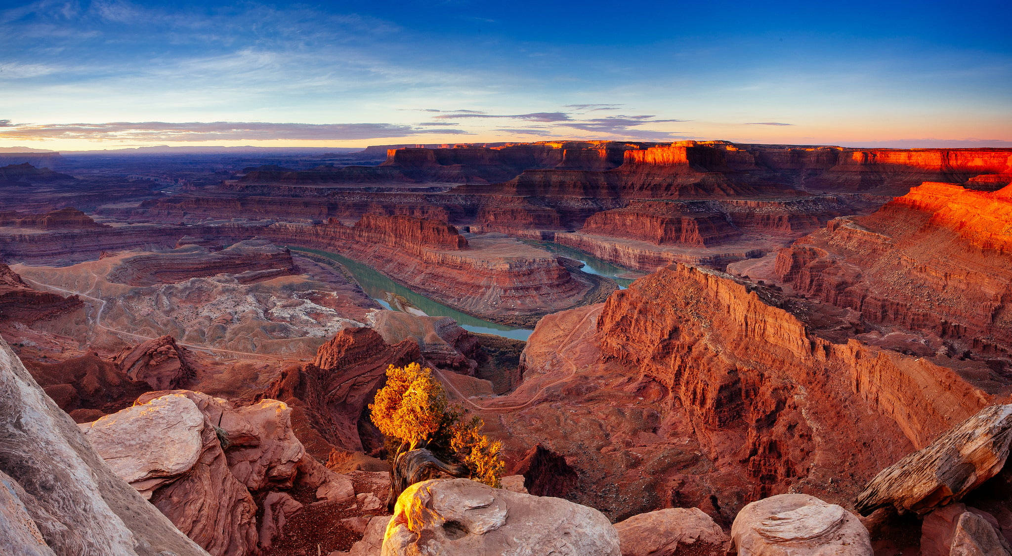 Canyonlands National Park 桌布 壁紙 — 令人嘆為觀止的日落將廣闊的峽谷沐浴在溫暖的橙色光芒中，蜿蜒的河流穿過崎嶇的紅色岩層。