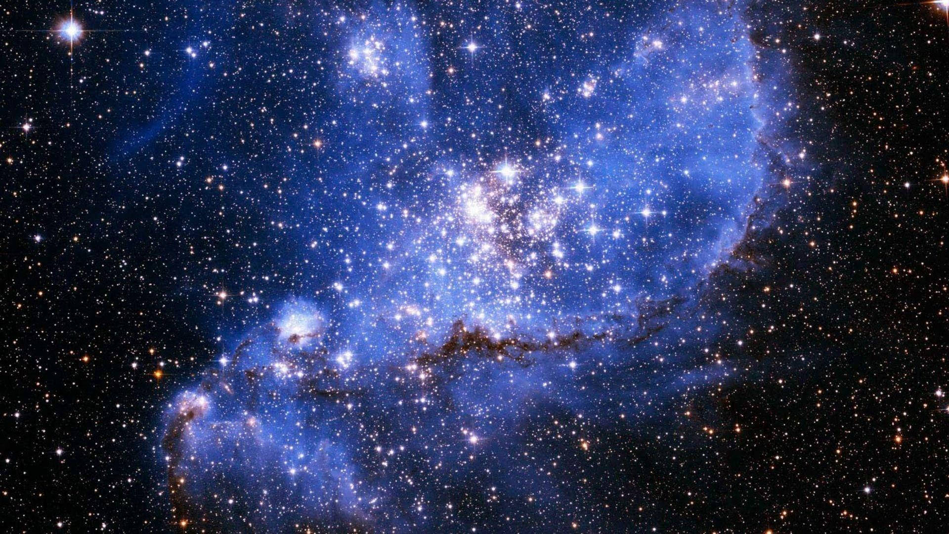 藍色銀河 桌布 壁紙 — 令人嘆為觀止的景象：一個發光的藍色星雲，充滿無數閃爍的星星，映襯著深邃的黑色宇宙虛空。