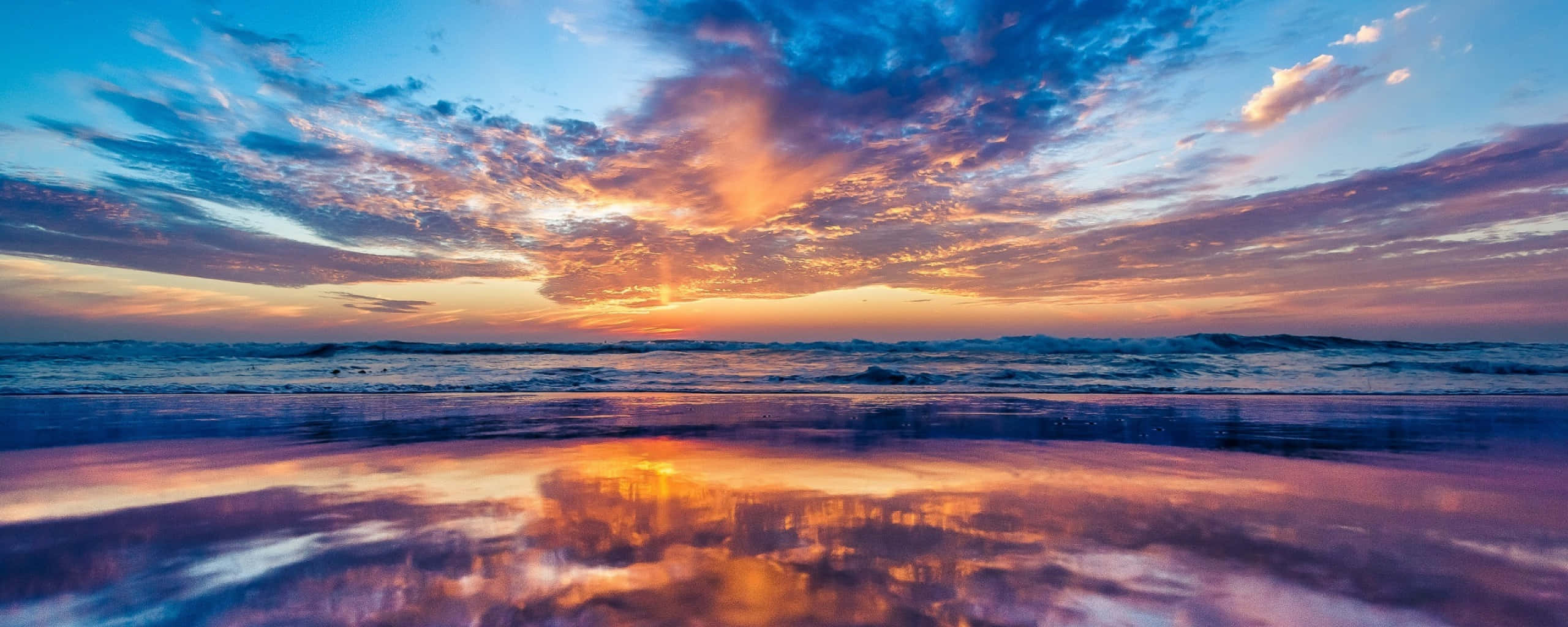 Sunset Ocean 桌布 壁紙 — 令人嘆為觀止的海上日落，火熱的橙色和紫色雲彩倒映在濕沙上。