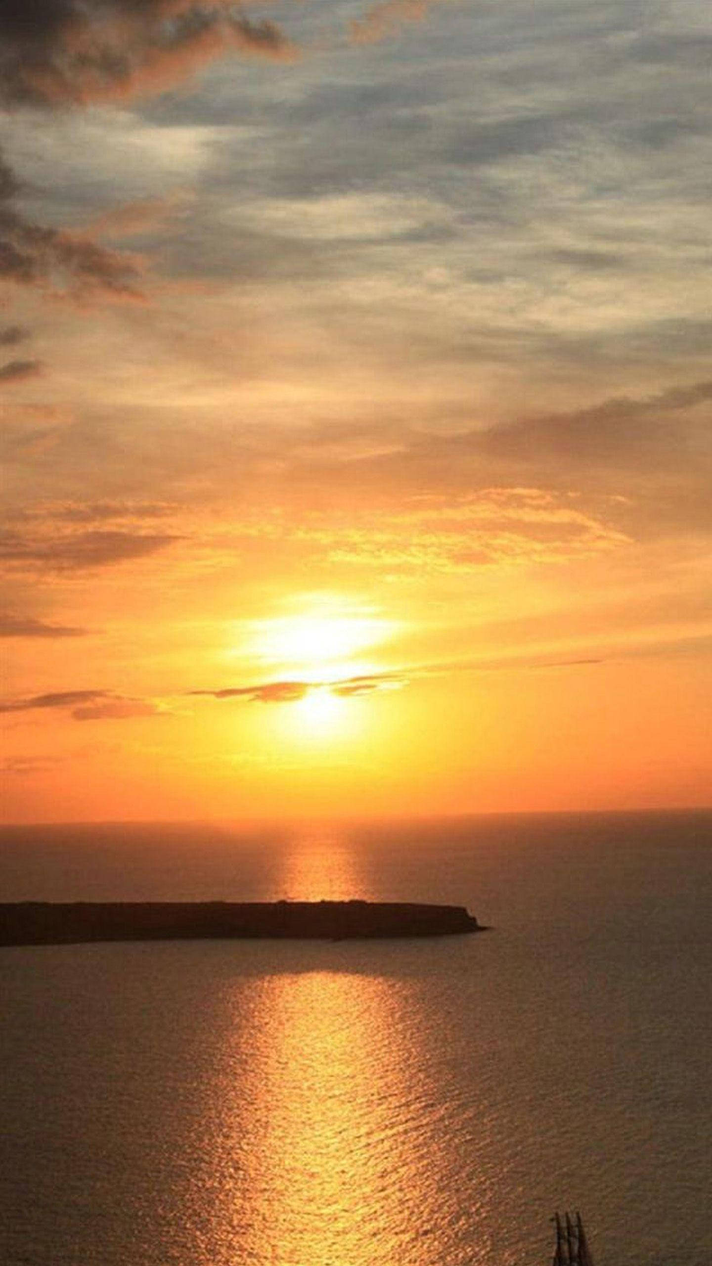 Ocean Sunset 桌布 壁紙 — 令人嘆為觀止的海上日落，金色的光芒在水面上反射，遠處的陸地在發光的天空下形成剪影。