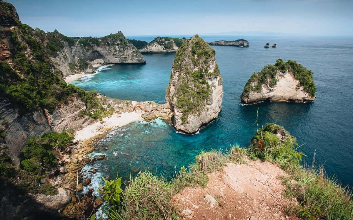 Bali Island 桌布 壁紙 — 令人嘆為觀止的海岸景觀，在清澈的藍天下，碧綠的海水拍打著崎嶇的懸崖和孤立的岩石 formations。