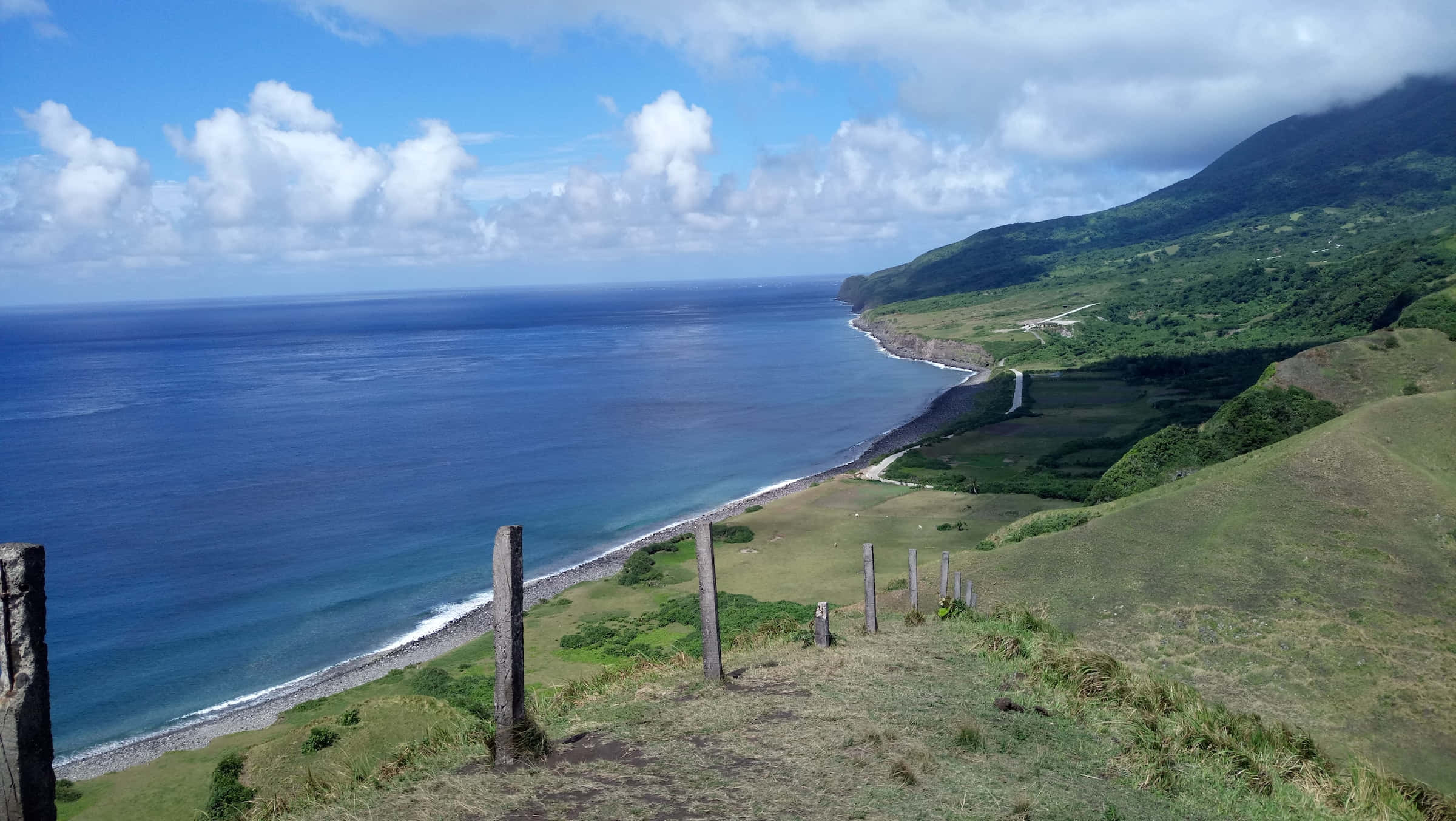 Best Nature 桌布 壁紙 — 令人嘆為觀止的海岸景觀，碧綠色的海洋與鬱鬱蔥蔥的綠色懸崖相接，上方是明亮的藍天，點綴著蓬鬆的白雲。