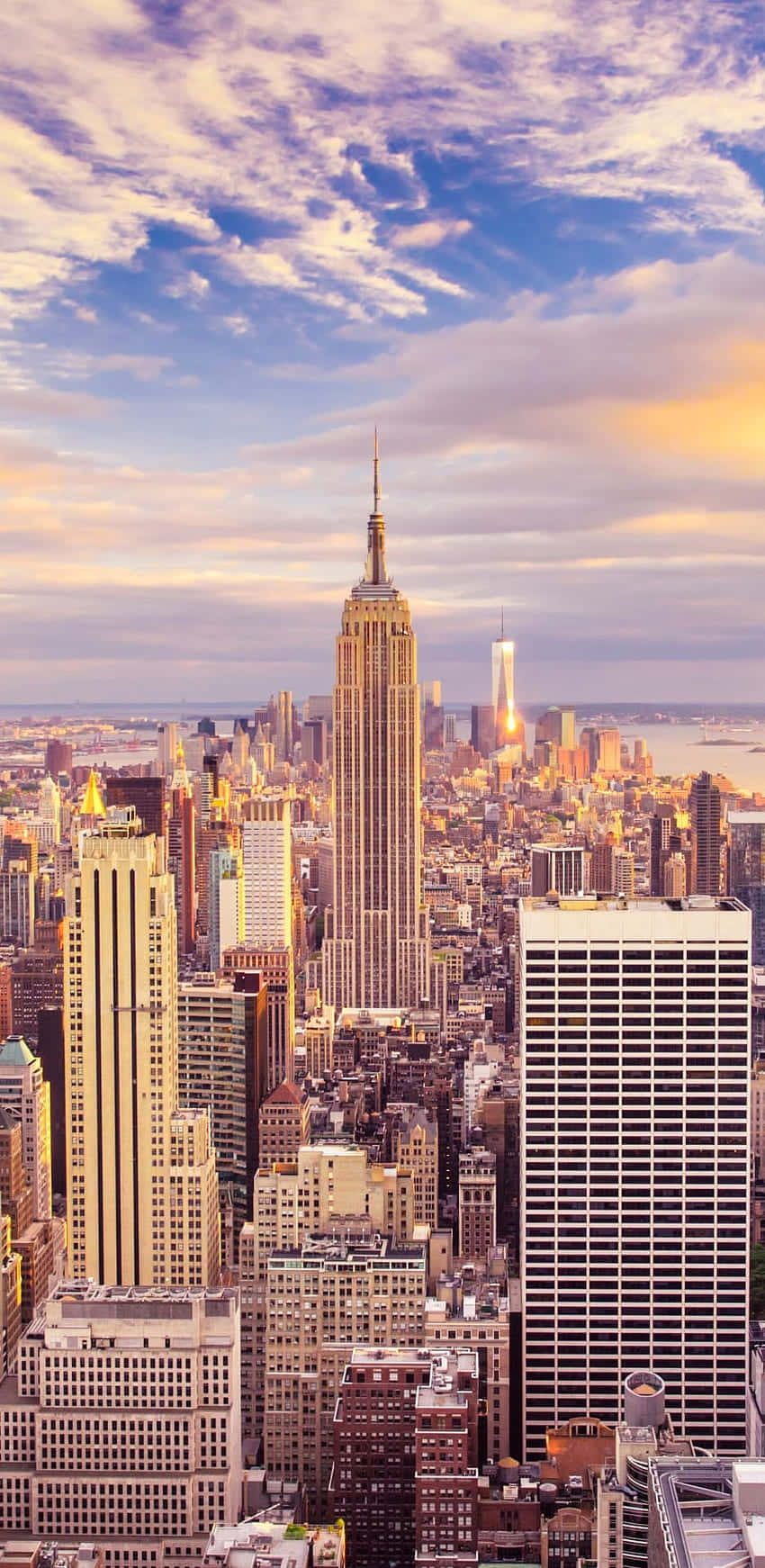 New York 桌布 壁紙 — 令人嘆為觀止的紐約市天際線日落景觀，以帝國大廈為主導，金色光芒照亮摩天大樓和雲層。
