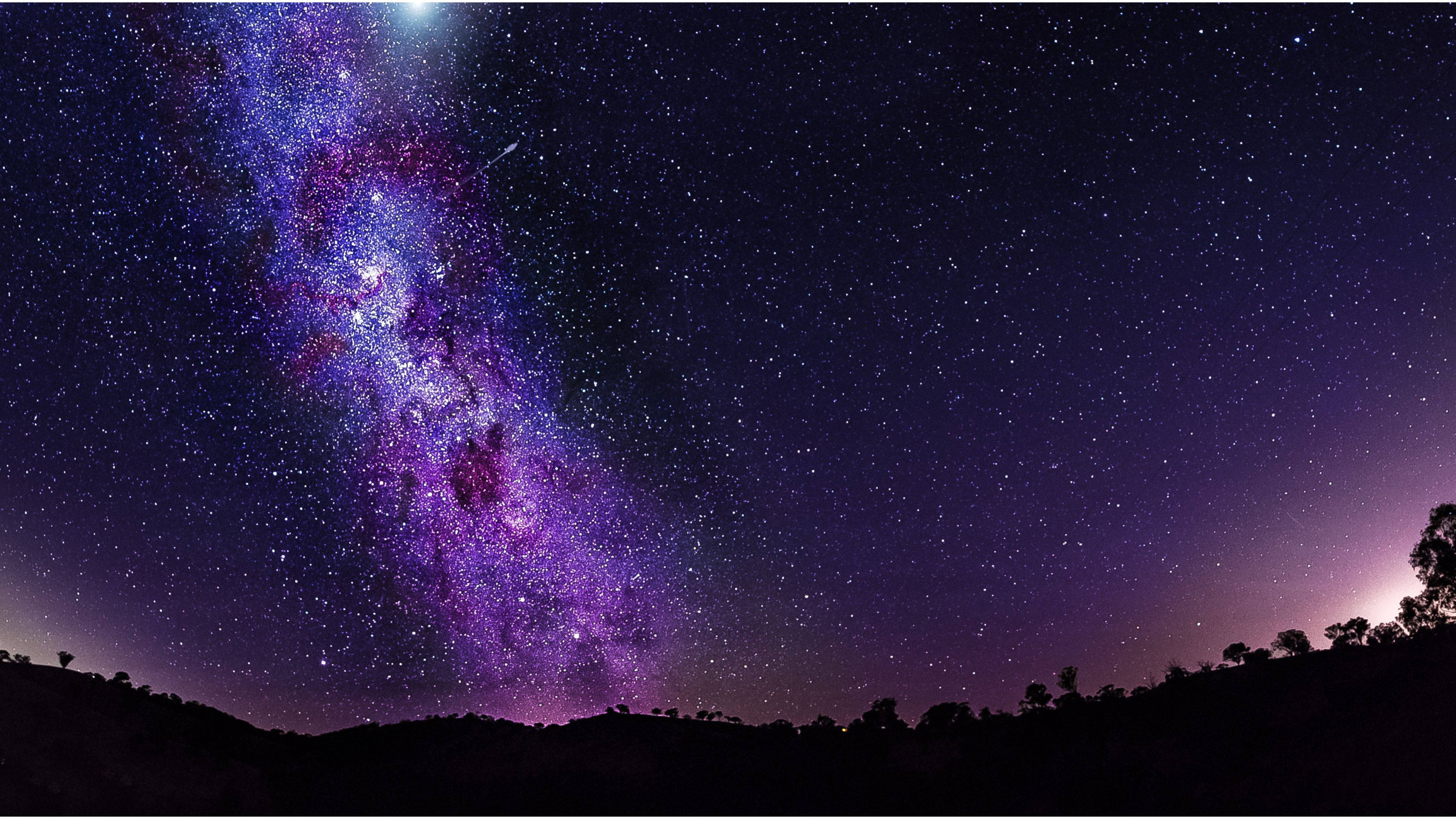 夜空 桌布 壁紙 — 令人嘆為觀止的銀河系景觀，在黑暗的山丘剪影上，在繁星點點的夜空下，散發著充滿活力的紫色和藍色色調。