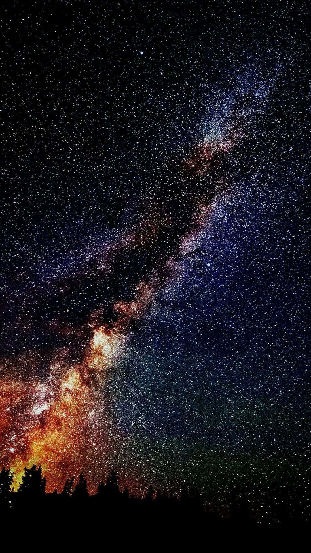 Cosmos 桌布 壁紙 — 令人嘆為觀止的銀河系景觀，在黑暗森林剪影上方閃爍著橙色和藍色色調。
