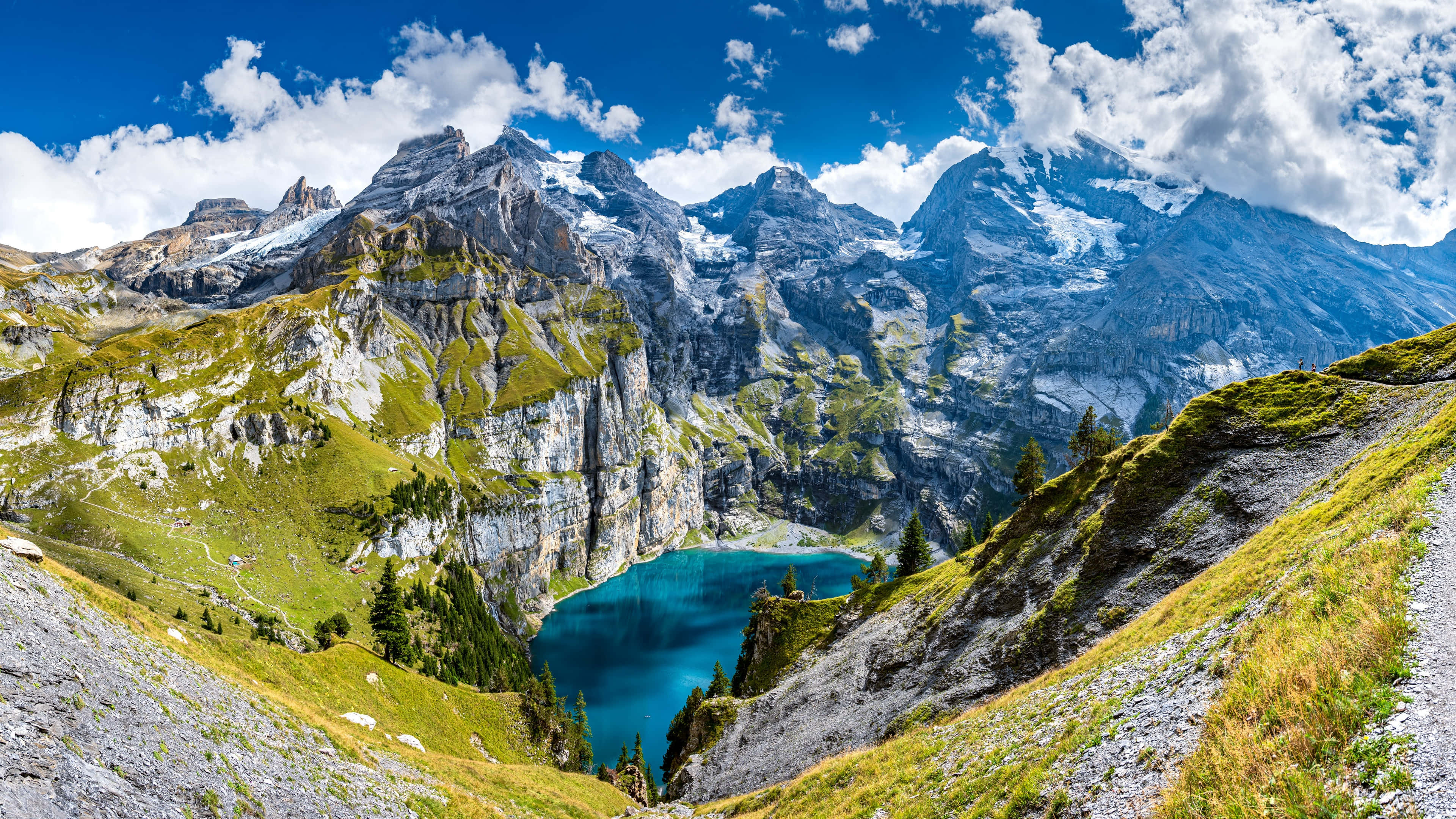 Beautiful Mountain Lake 桌布 壁紙 — 令人嘆為觀止的阿爾卑斯山全景，在明亮的藍天和蓬鬆的白雲下，一個充滿活力的綠松石湖坐落在高聳的雪山之間。
