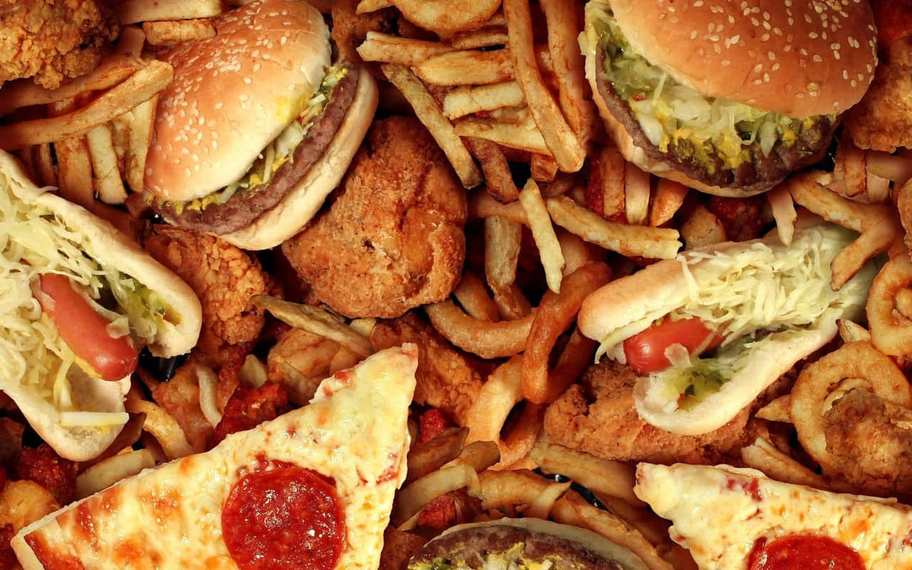 Fries 桌布 壁紙 — 令人垂涎欲滴的特寫鏡頭，各種快餐堆疊得高高的，有漢堡、薯條、熱狗和披薩片。