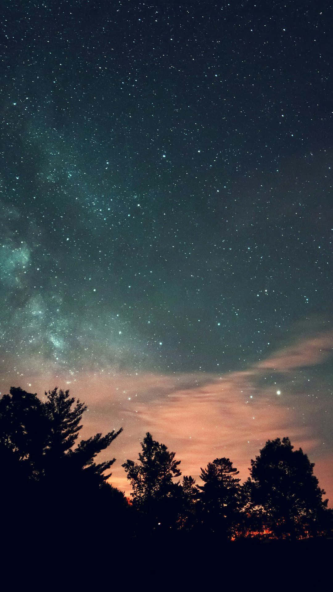 Aesthetic Night Sky 桌布 壁紙 — 令人屏息的夜空，佈滿無數星星，銀河在剪影松樹上方拱起，背景是藍綠色和橙色雲彩的漸變。