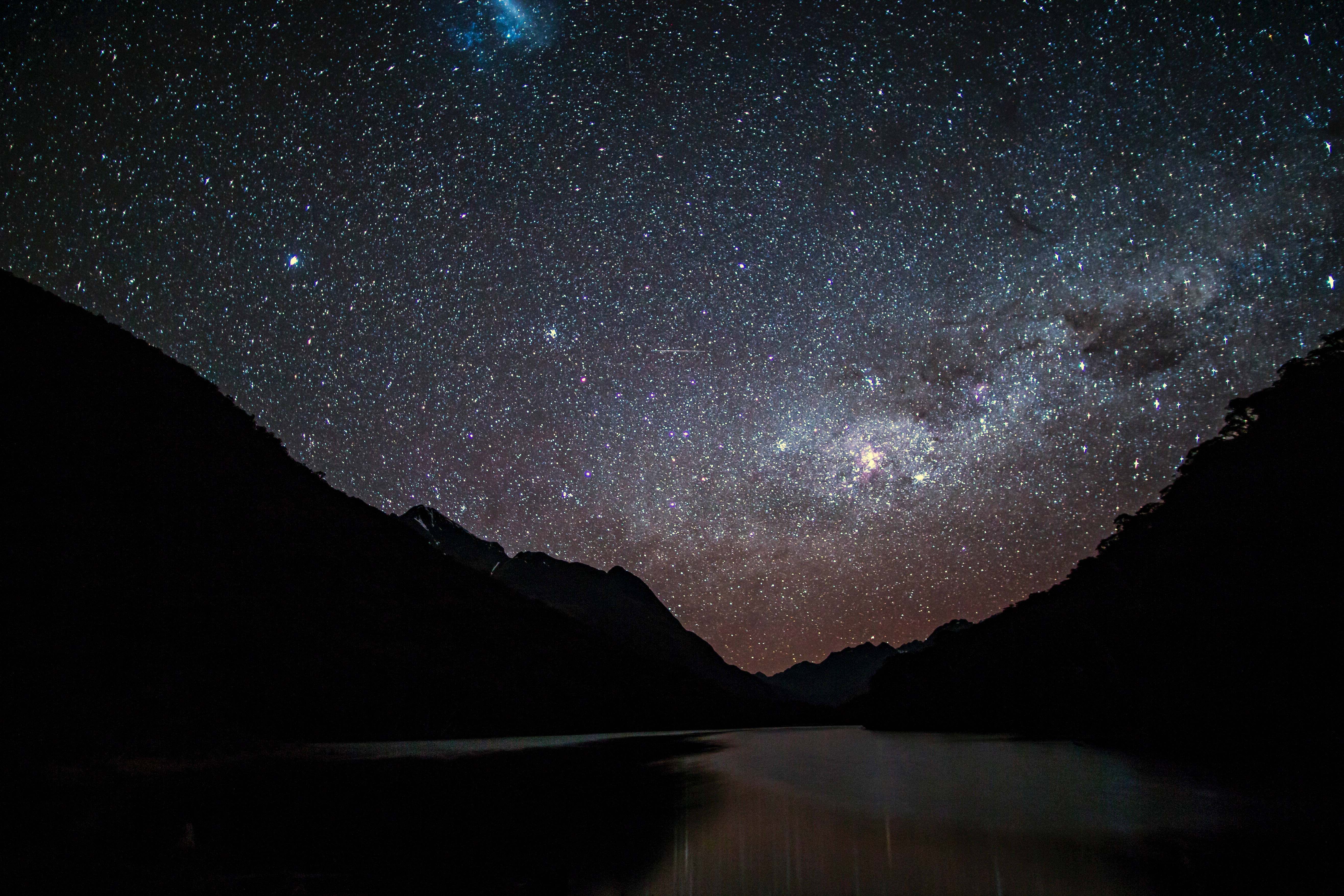 Starry 桌布 壁紙 — 令人屏息的夜空，佈滿無數星辰，銀河在黑暗山巒剪影之間的平靜湖泊上空拱起。