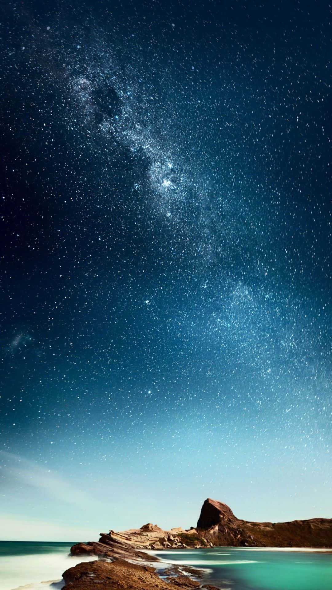 海灘 桌布 壁紙 — 令人屏息的夜空，佈滿無數星辰，銀河在寧靜的碧綠海洋和岩石海岸線上拱起。