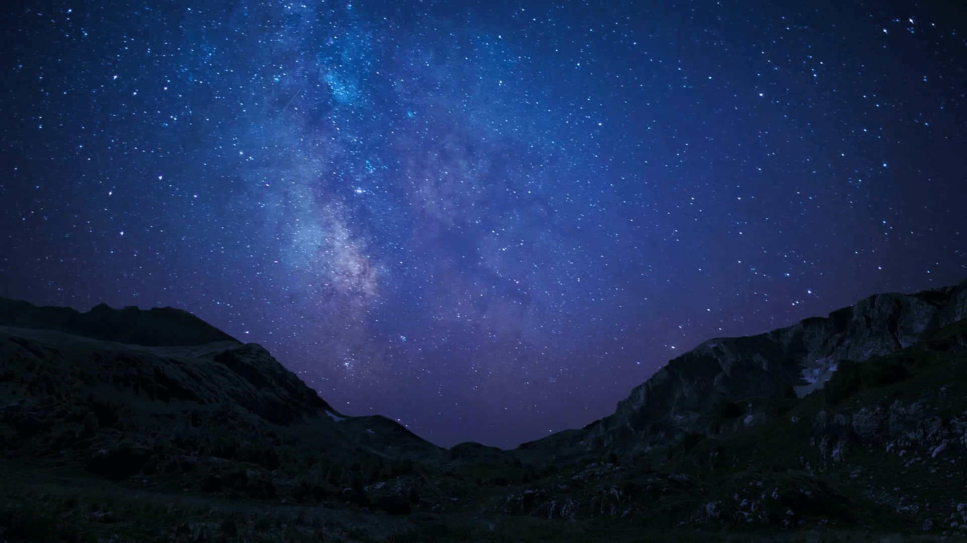 夜空 桌布 壁紙 — 令人屏息的夜空，佈滿無數星辰，閃耀的銀河在黑暗崎嶇的山峰上彎曲延伸。