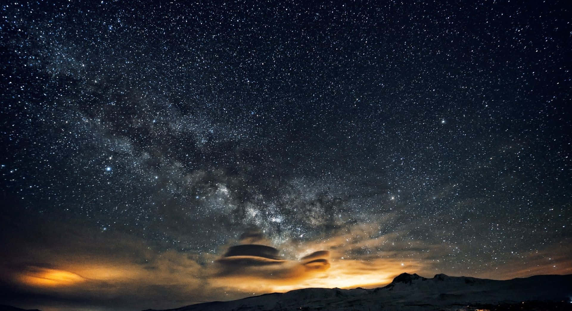 Beautiful Sky 桌布 壁紙 — 令人屏息的夜空，佈滿無數繁星，銀河在積雪的山峰上拱起，下方是發光的橙色雲層。