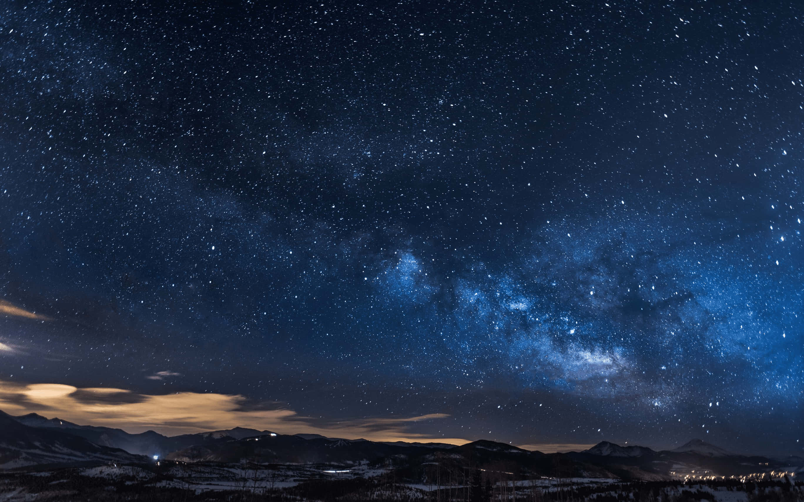 Starry 桌布 壁紙 — 令人屏息的夜空，充滿無數星星，發光的銀河拱起在積雪的山脈上，下方有遠方的燈光。