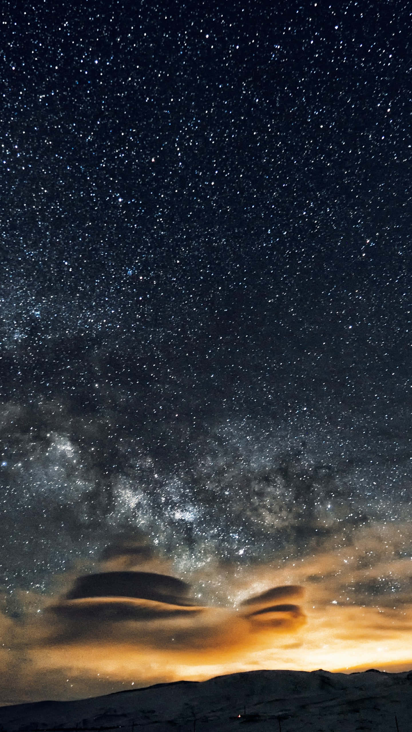 直式 桌布 壁紙 — 令人屏息的夜空，充滿無數星星和銀河，在發光的橙色雲層下拱形跨越積雪覆蓋的山脈。
