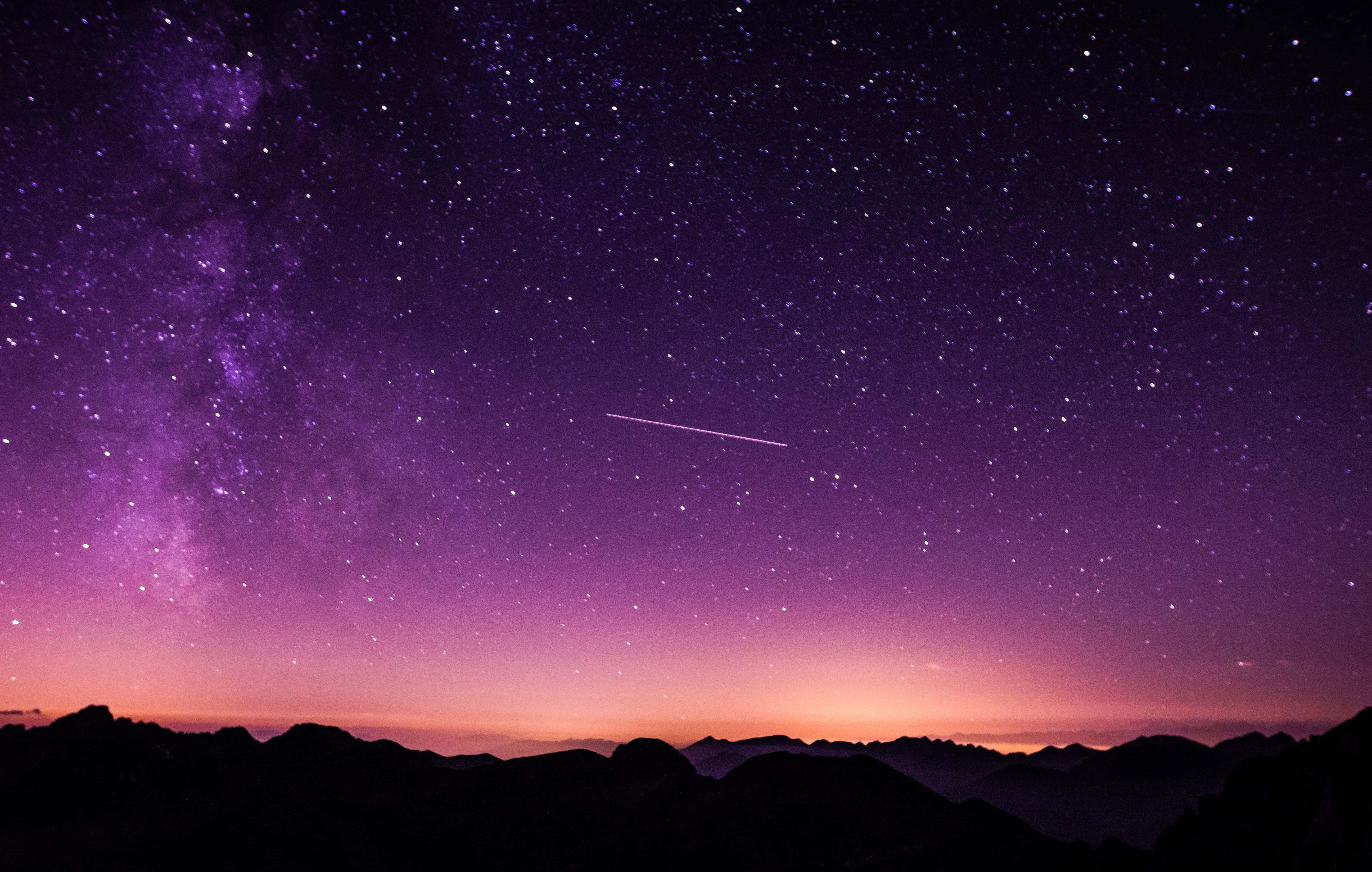 夜空 桌布 壁紙 — 令人屏息的夜空，山巒剪影在紫色和粉紅色調中閃耀，一顆明亮的流星劃過銀河。