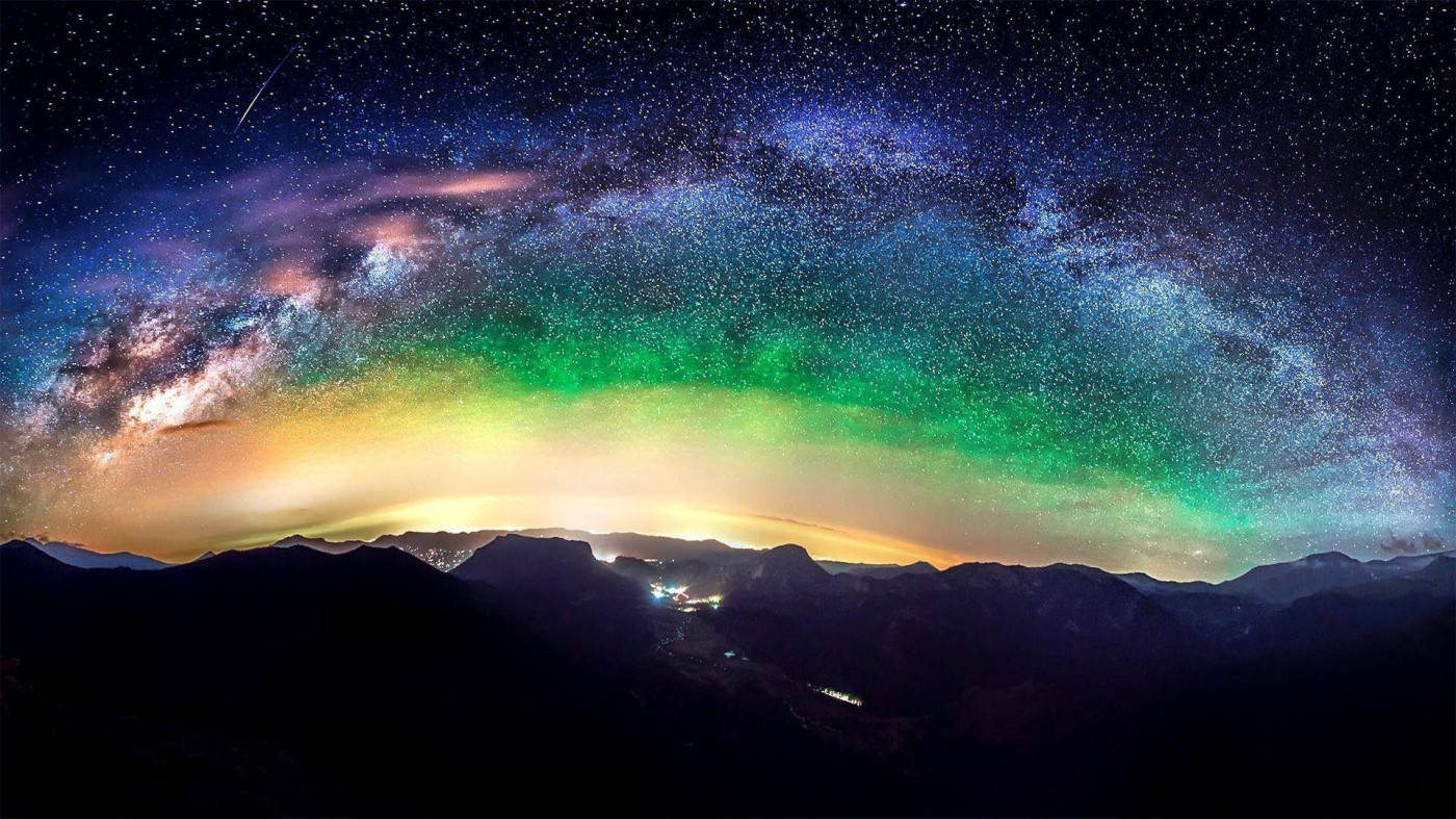 山景 桌布 壁紙 — 令人屏息的夜空籠罩著山巒剪影，銀河與北極光以鮮豔的綠色和紫色閃耀。