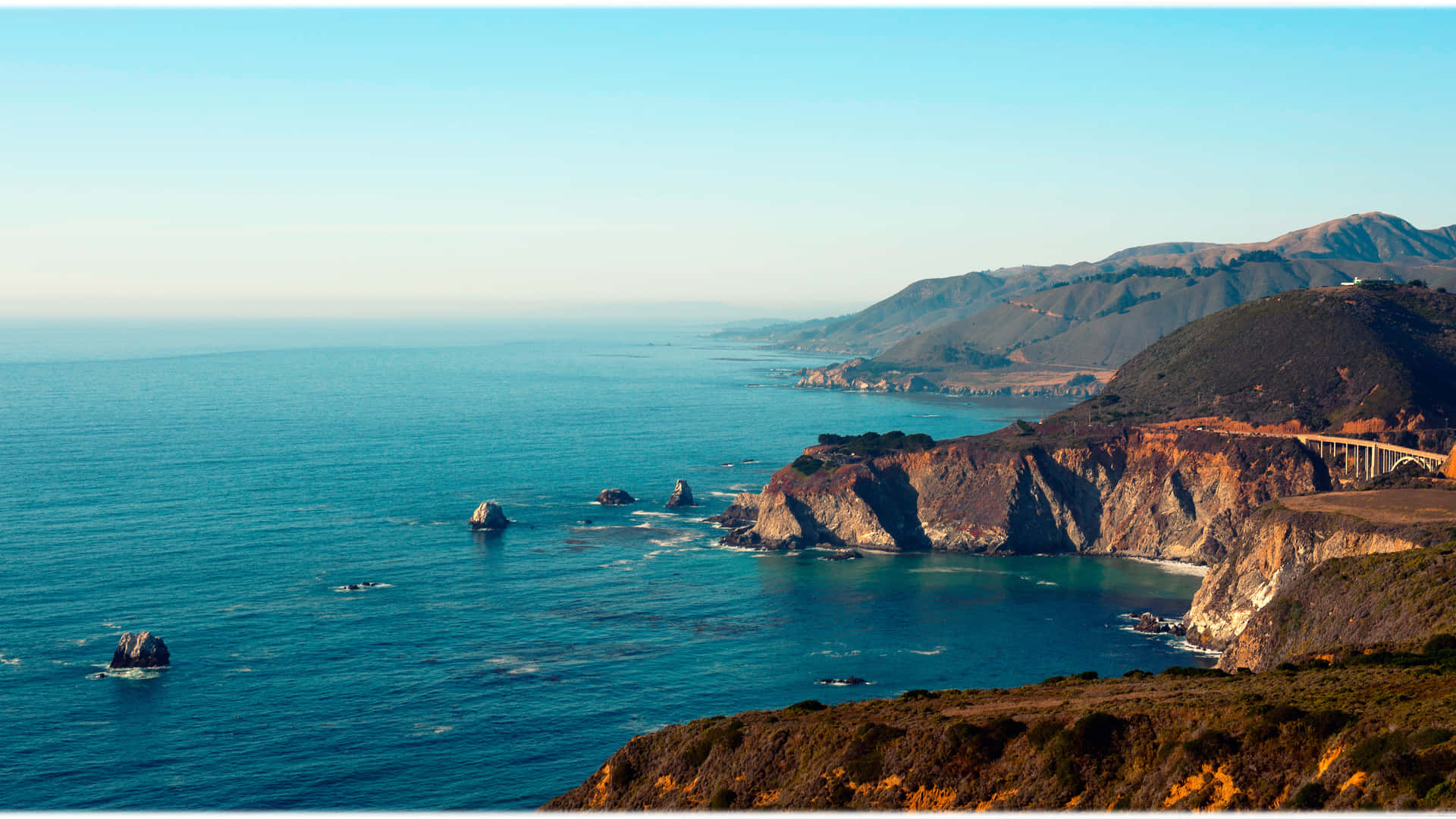 macOS Big Sur 動態桌布 桌布 壁紙 — 令人屏息的海岸景觀，碧綠的海浪拍打著崎嶇的懸崖和遠山，天空清澈湛藍。
