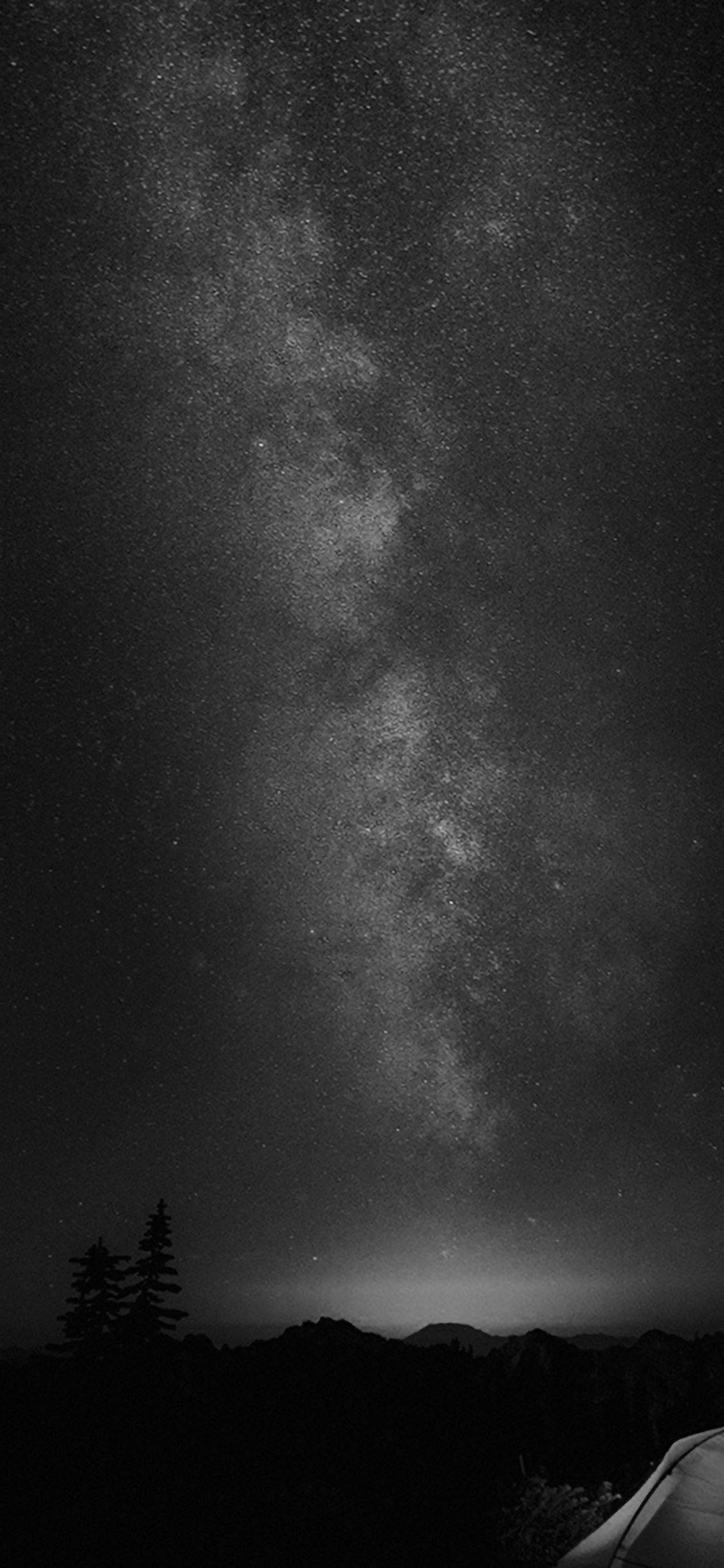 black apple iPhone 桌布 壁紙 — 令人屏息的黑白夜空，佈滿密集的星星，銀河在黑暗的山巒輪廓和帳篷上方拱起。