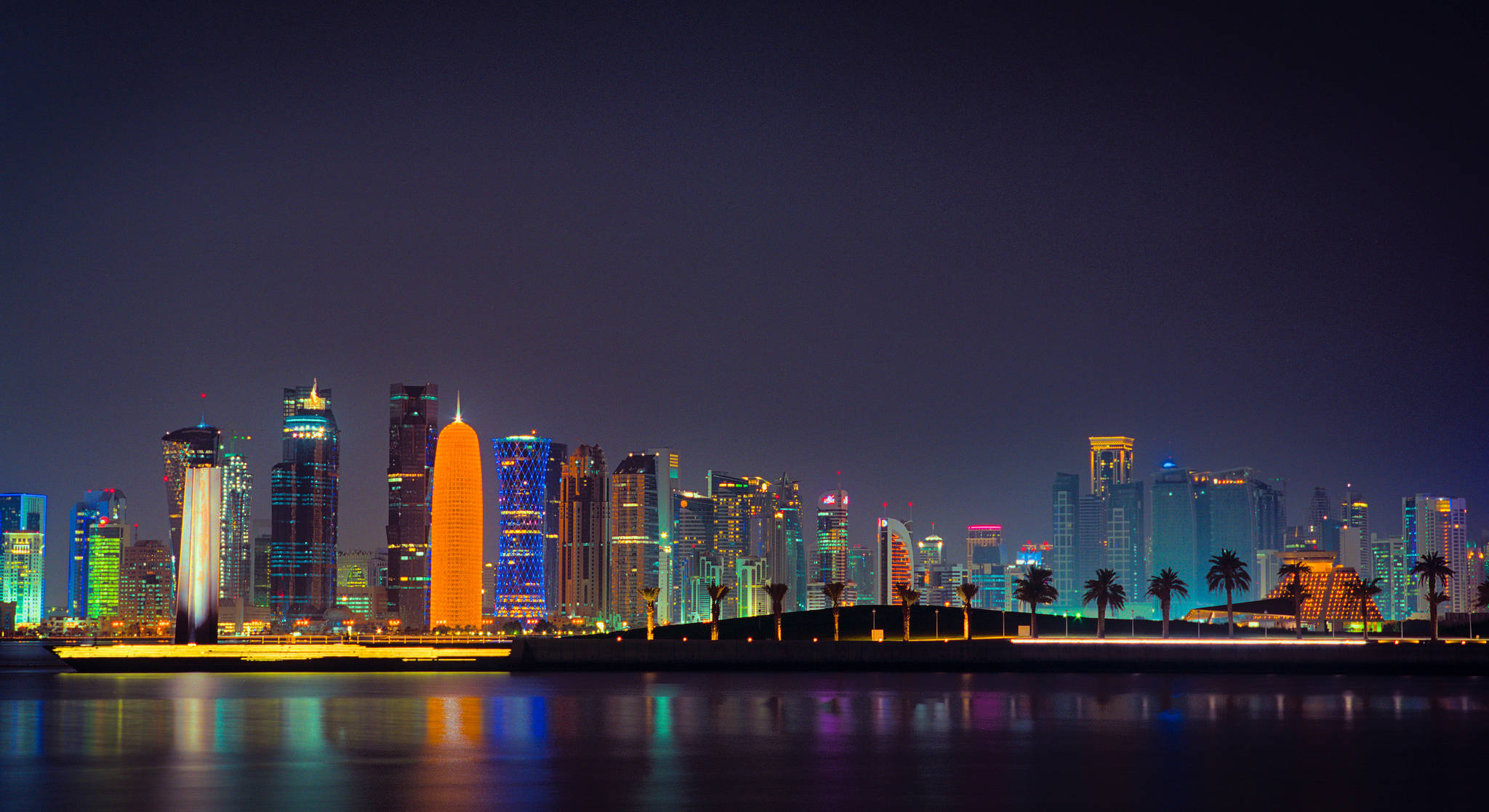 Qatar 桌布 壁紙 — 令人目眩的夜景城市景觀，摩天大樓在霓虹色調中閃耀，倒映在平靜的水面上。