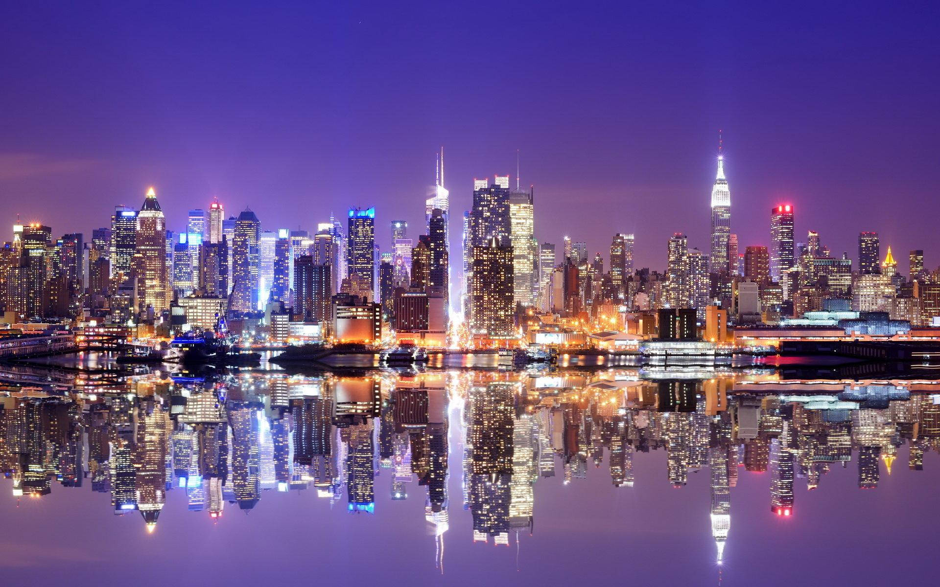 Skyscraper 桌布 壁紙 — 令人目眩的夜景城市景觀，摩天大樓在深紫色天空下閃耀，完美倒映在下方平靜的水面上。