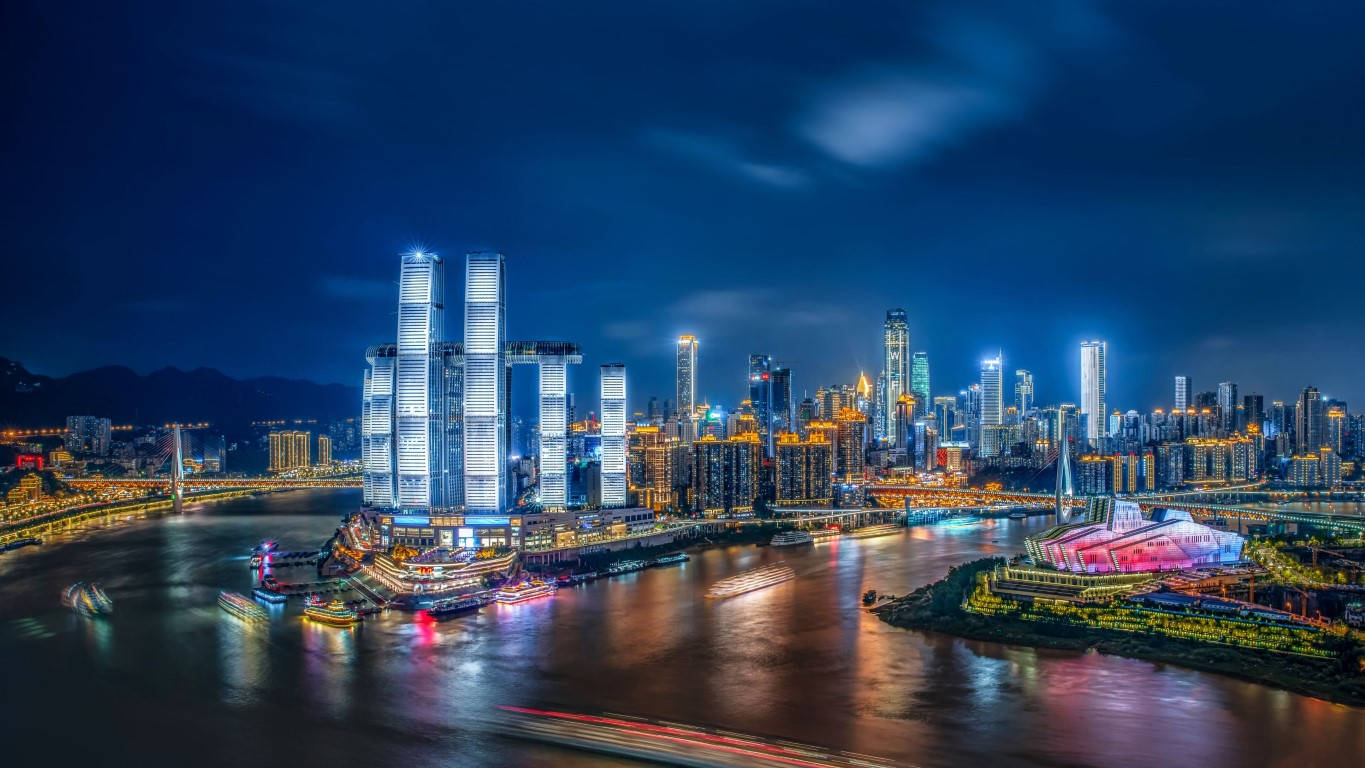 Chongqing 桌布 壁紙 — 令人目眩的夜景城市景觀，燈火通明的摩天大樓倒映在河面上，伴隨著船隻留下的光跡。