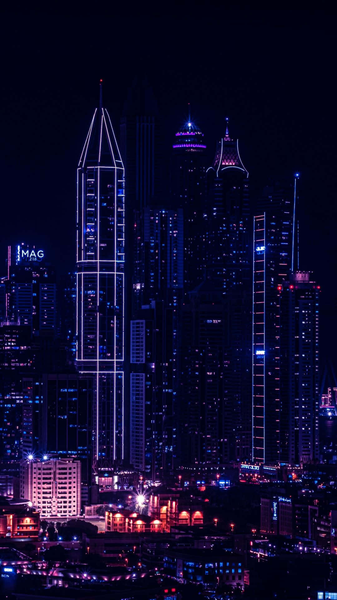 城市風景 桌布 壁紙 — 令人目眩的夜景城市景觀，高聳的摩天大樓在深黑色的天空映襯下閃耀著電光藍和紫色霓虹燈光。