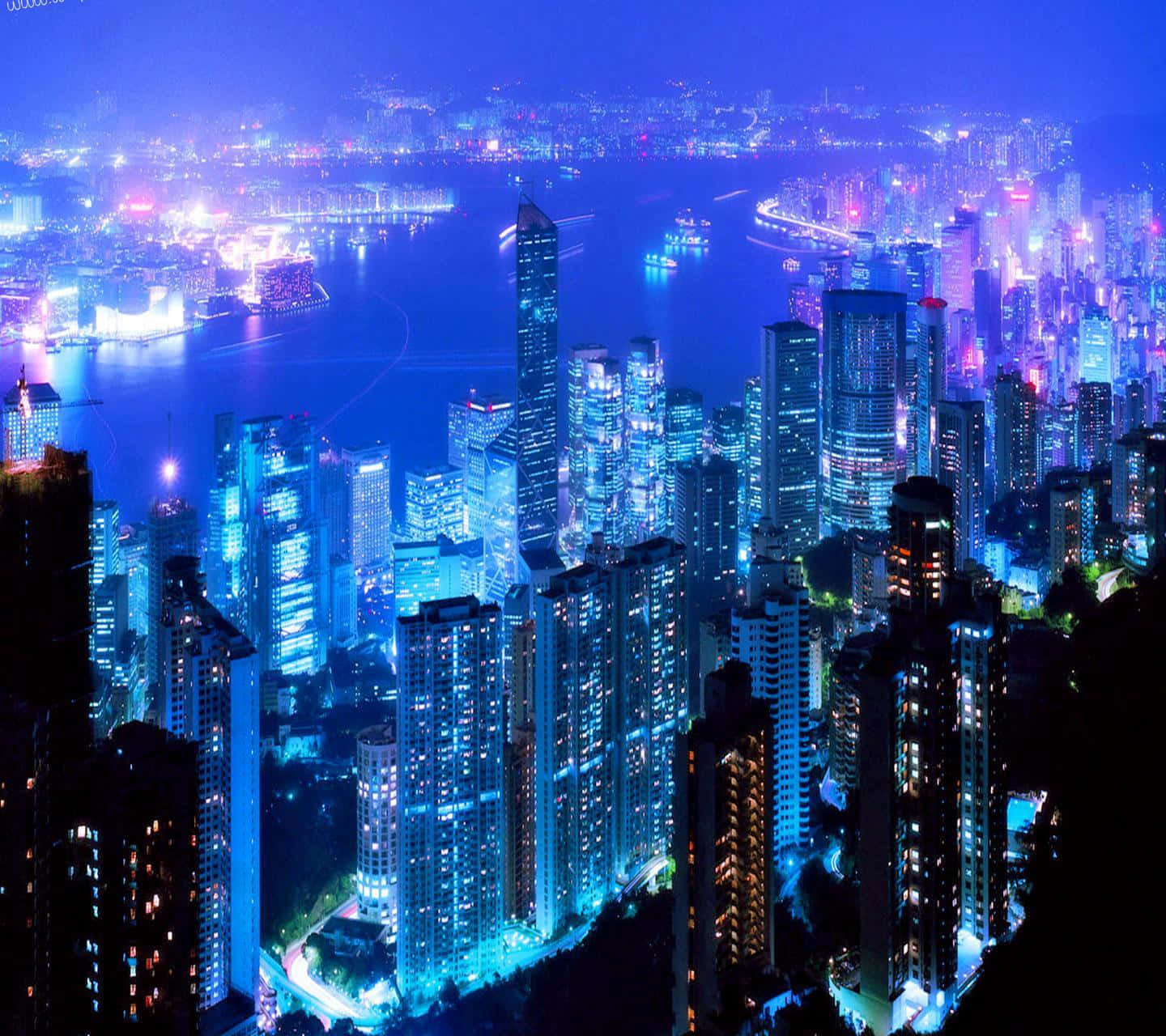 3d City 桌布 壁紙 — 令人眼花撩亂的夜景，高聳的摩天大樓沿著充滿活力的海濱閃爍著藍色和紫色的燈光。