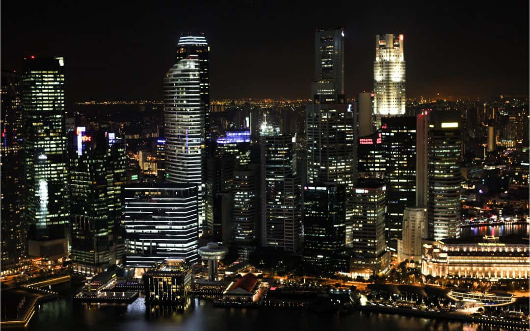 Night Time 桌布 壁紙 — 令人眼花撩亂的夜景，高聳的摩天大樓在黑暗的水道上閃爍著倒映的燈光。