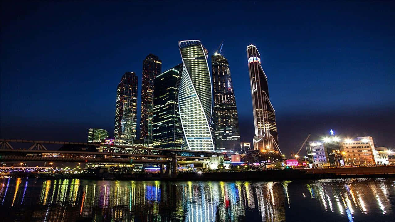 Russia 桌布 壁紙 — 令人眼花撩亂的現代摩天大樓夜景，璀璨燈光倒映在平靜的河面上。