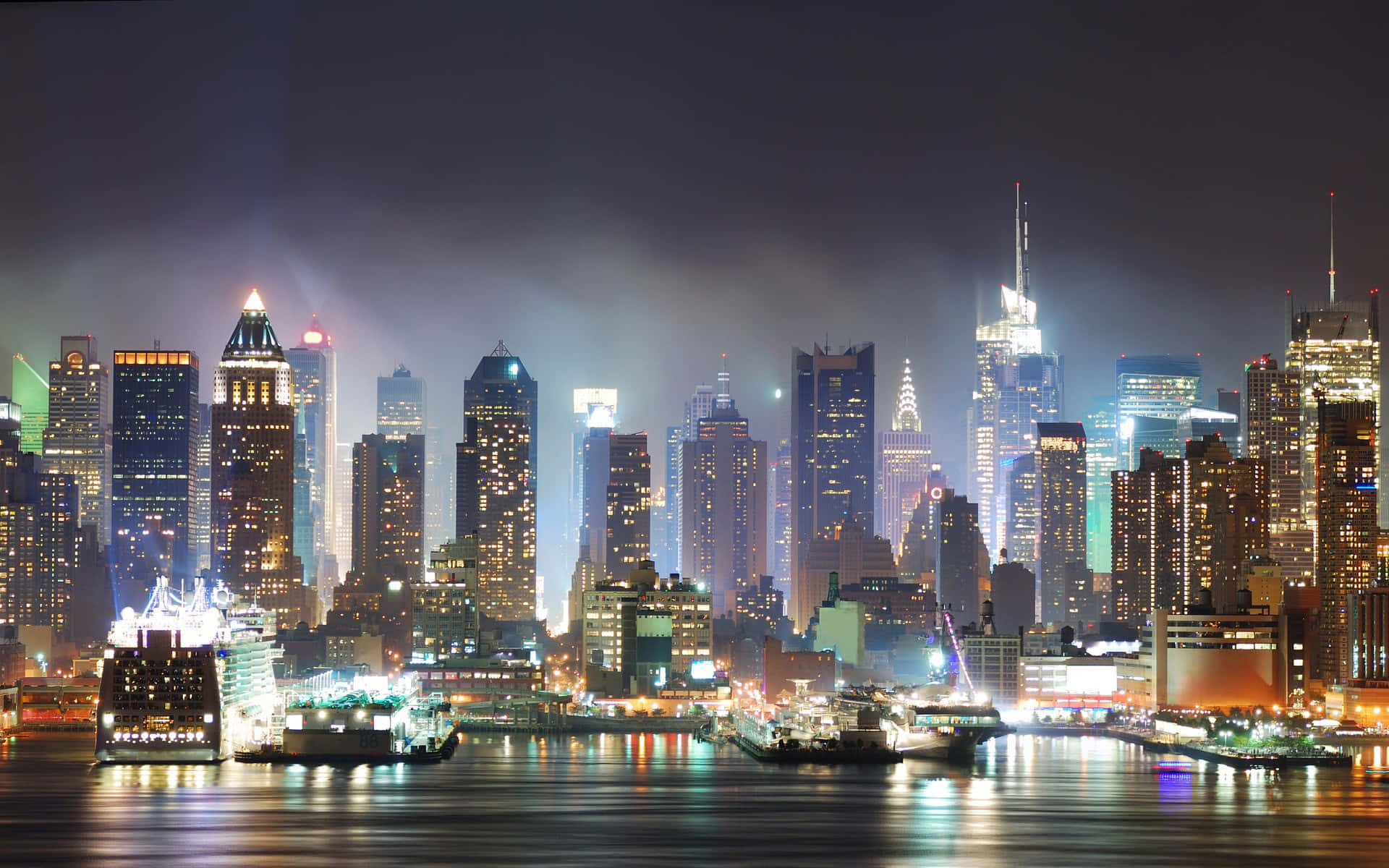 3d City 桌布 壁紙 — 令人眼花繚亂的夜景，高聳的摩天大樓在平靜的水面上閃爍著燈光倒影。