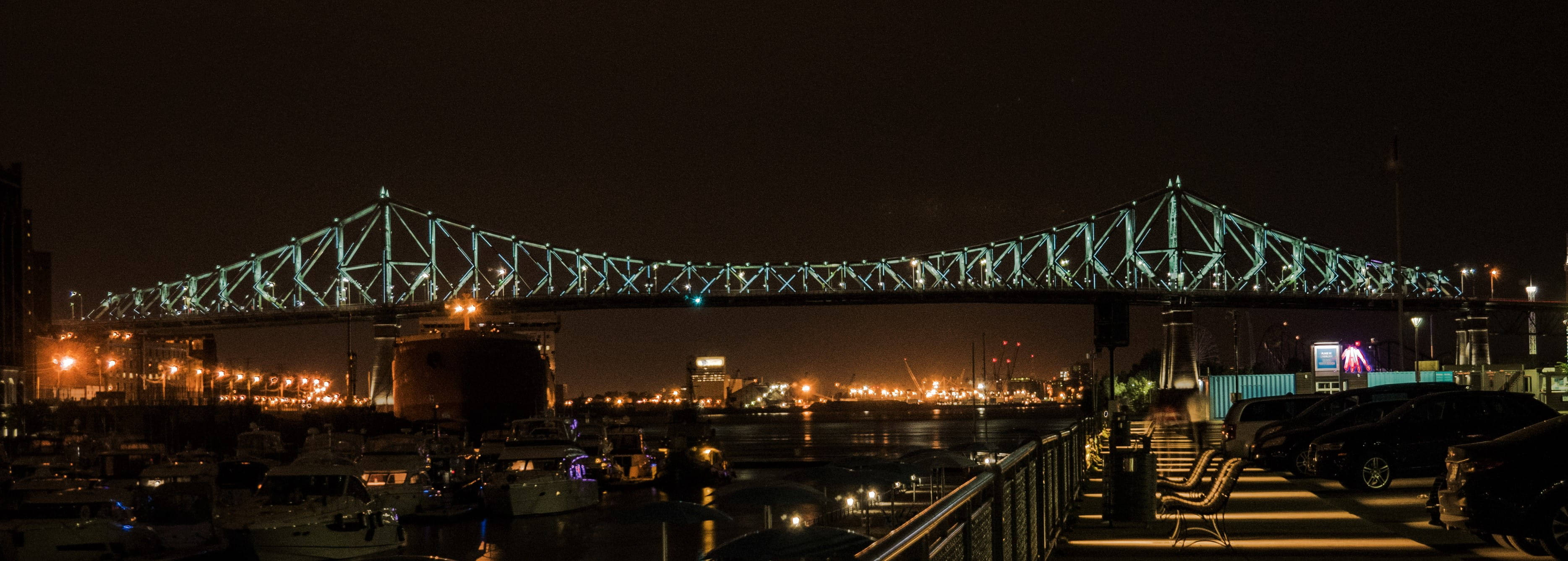 Montreal 桌布 壁紙 — 令人驚嘆的夜景，一座亮燈的鋼桁架橋橫跨港口，船隻和城市燈光倒映在水面上。