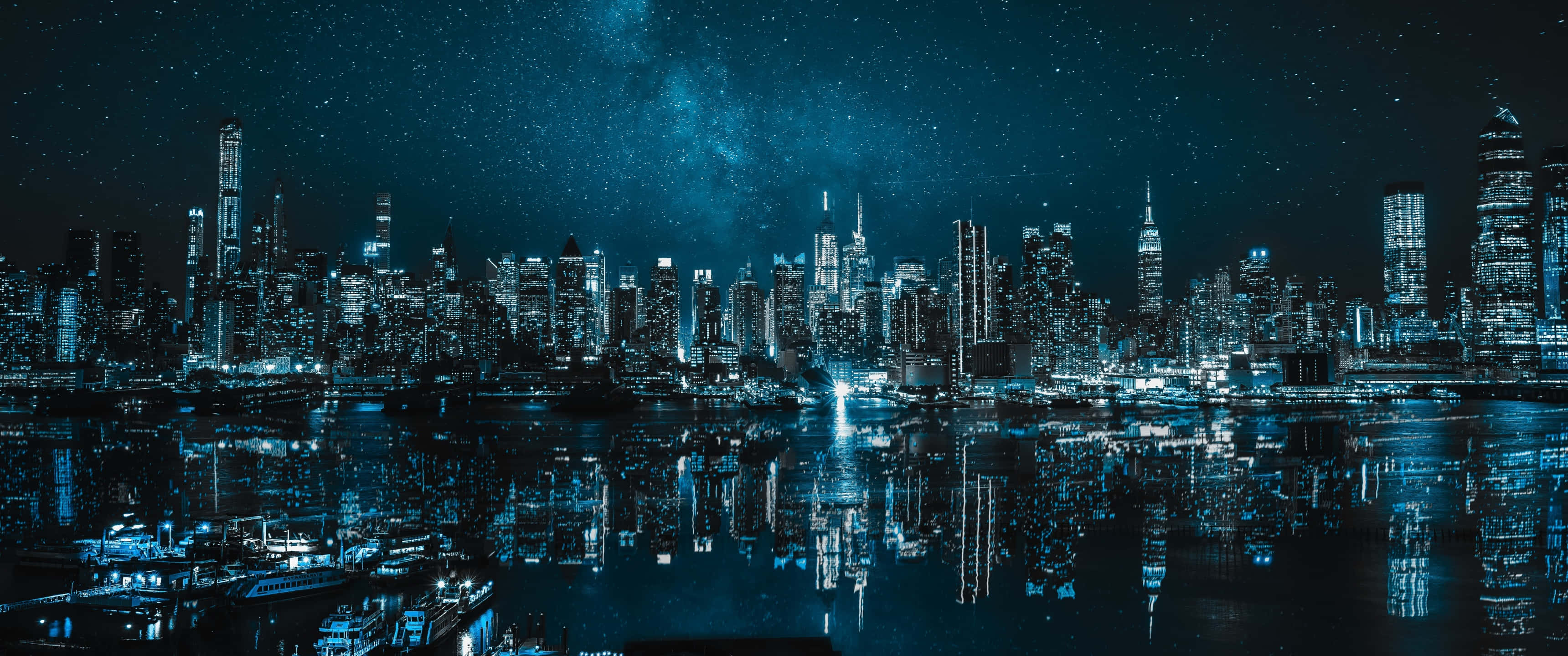 City Night 桌布 壁紙 — 令人驚嘆的夜景，摩天大樓在星空和銀河映照下閃爍，倒映在黑暗的水面上。