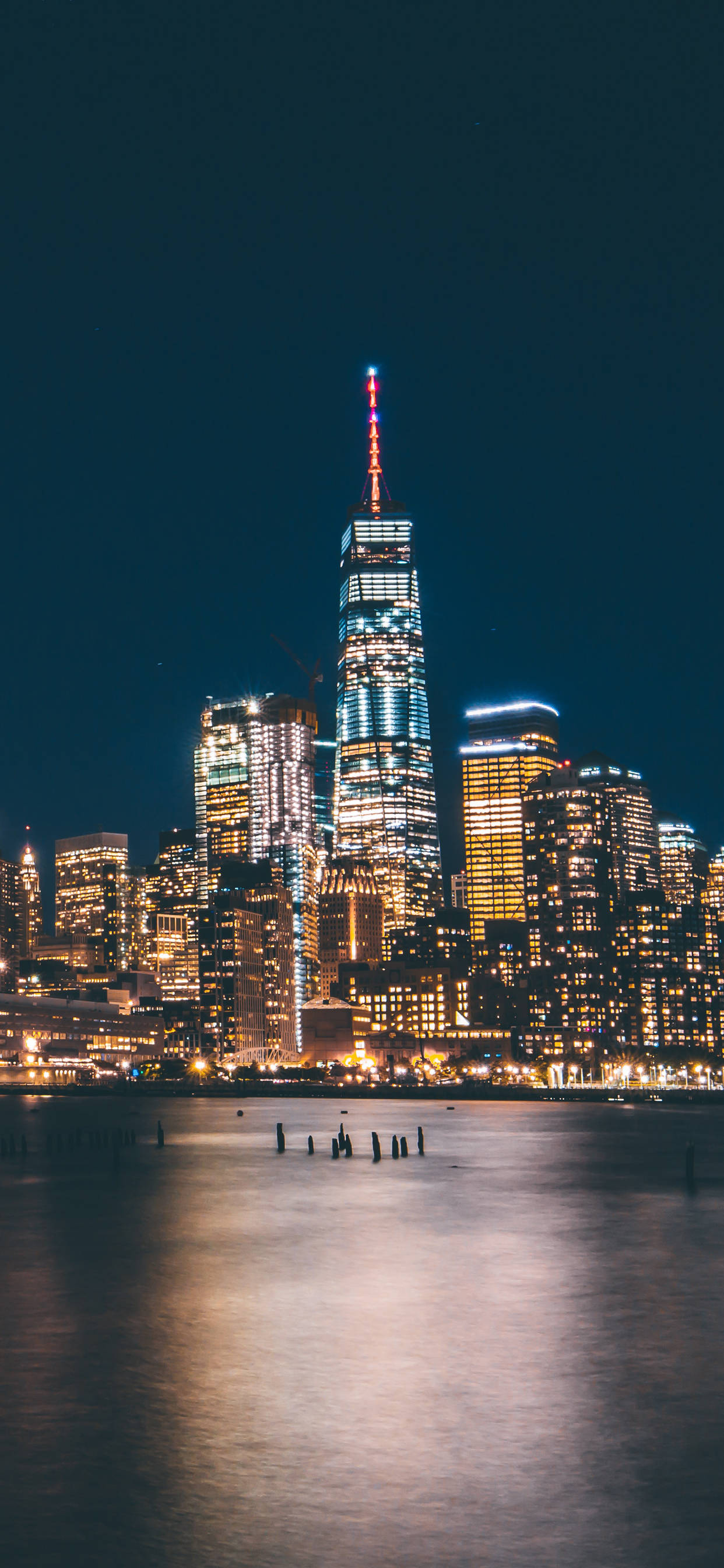New York 桌布 壁紙 — 令人驚嘆的夜景，照亮了世界貿易中心一號大樓及周圍摩天大樓，倒映在平靜的水面上。