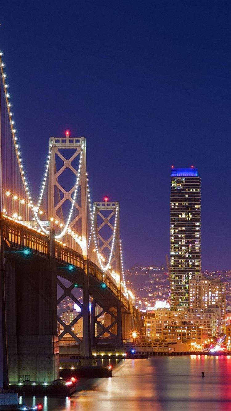 san francisco iPhone 桌布 壁紙 — 令人驚嘆的夜景，照亮的海灣大橋和高聳的摩天大樓倒映在平靜的水面上。