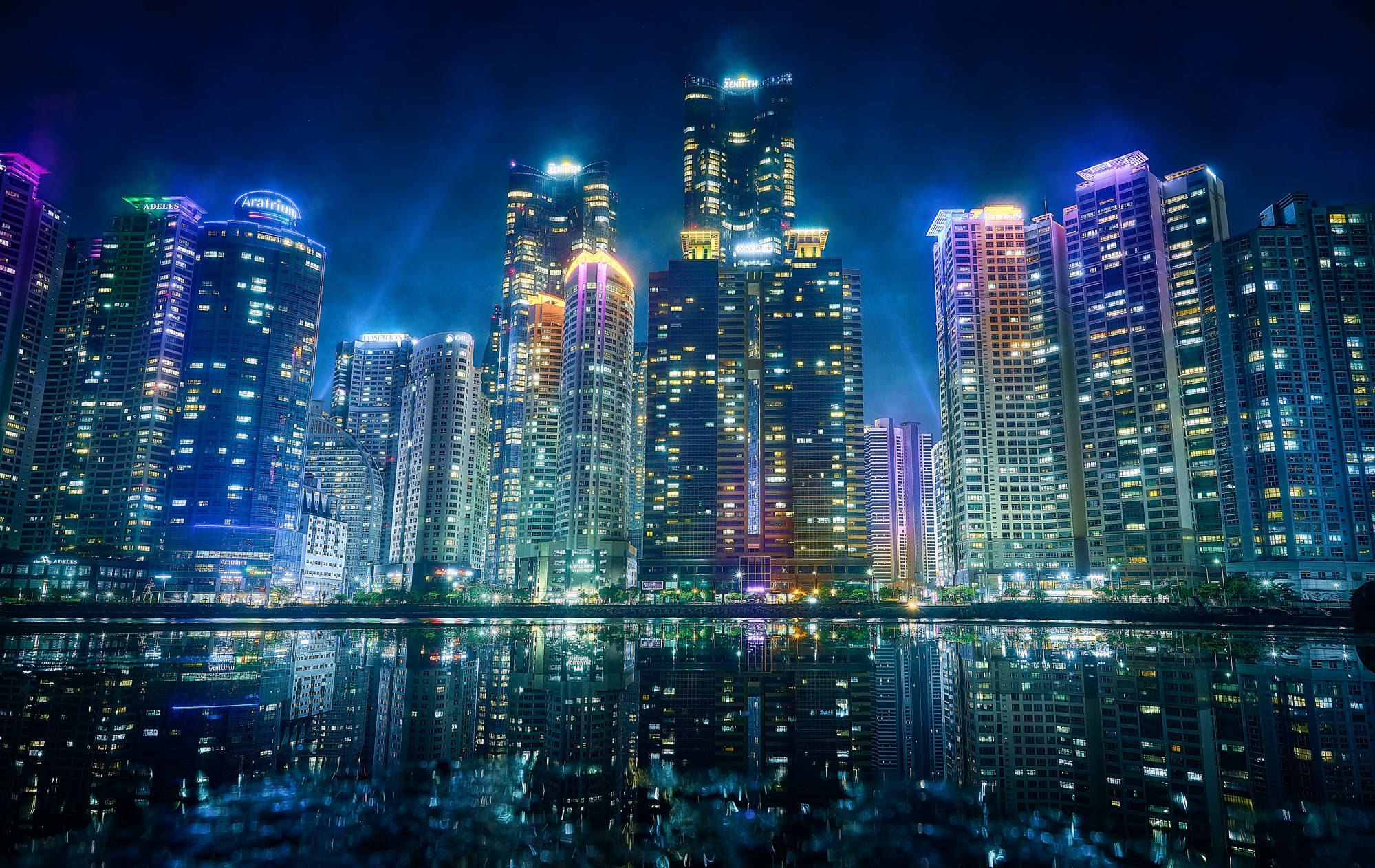 Busan 桌布 壁紙 — 令人驚嘆的夜景，高聳的摩天大樓與鮮豔的霓虹燈完美倒映在平靜的水面上。