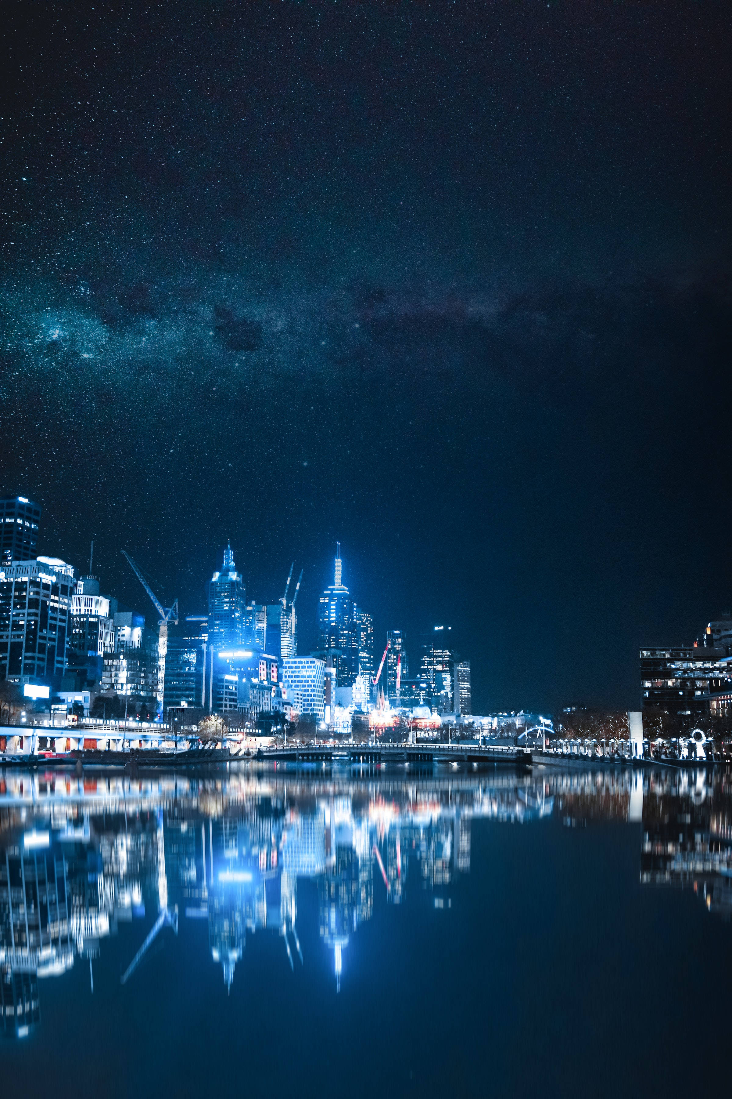 夜空 桌布 壁紙 — 令人驚嘆的夜景城市景觀，摩天大樓在平靜的水面上倒映，星空下可見銀河。