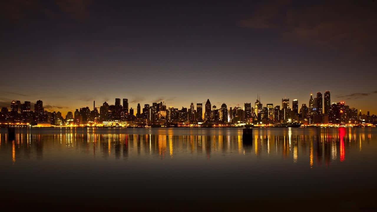 720p Ny City 桌布 壁紙 — 令人驚嘆的夜景城市景觀，摩天大樓在暮色天空中閃耀，它們的燈光完美地倒映在平靜的水面上。