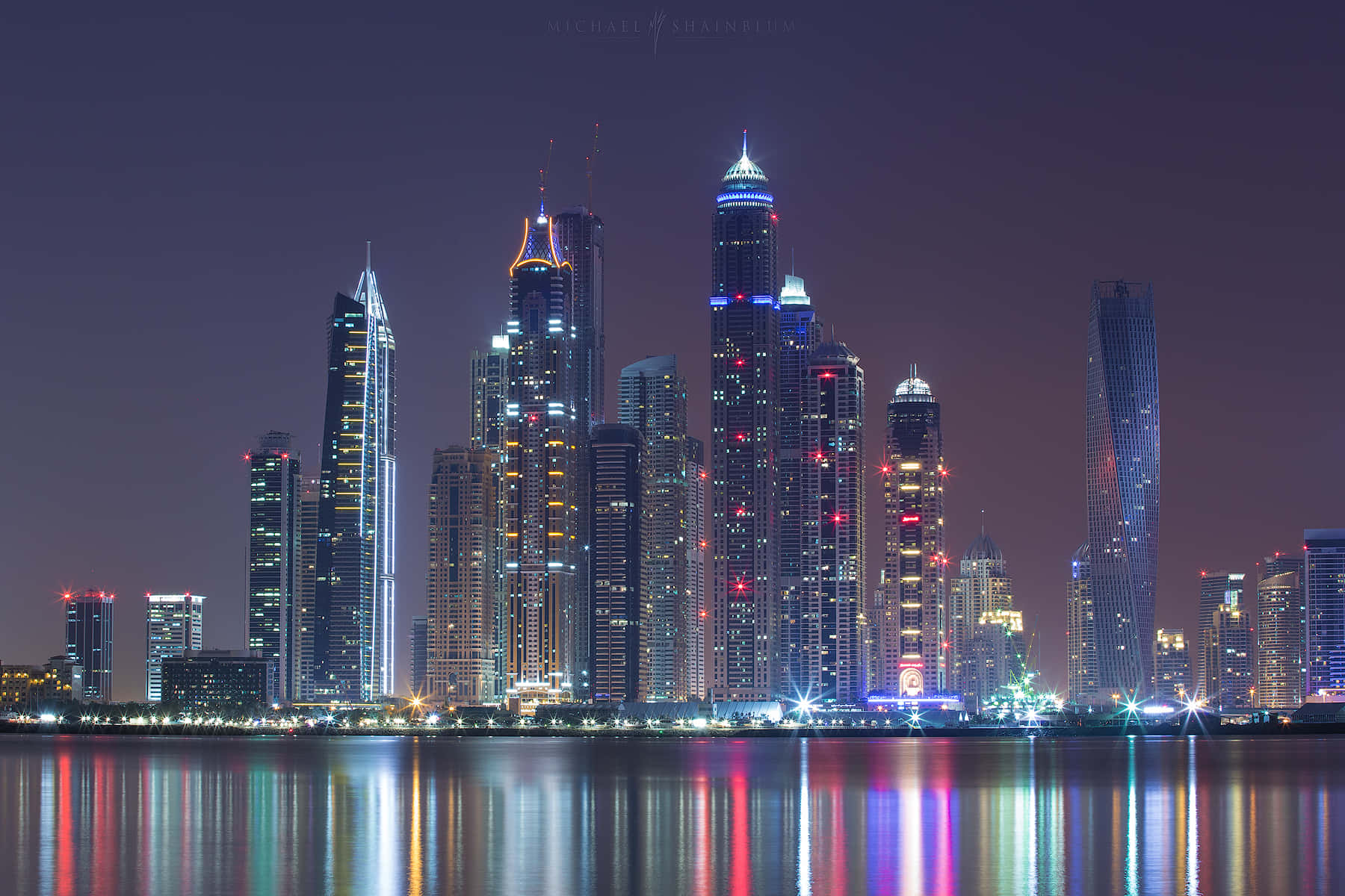 杜拜 桌布 壁紙 — 令人驚嘆的夜景城市景觀，高聳的摩天大樓在平靜的水面上反射出鮮豔的燈光。