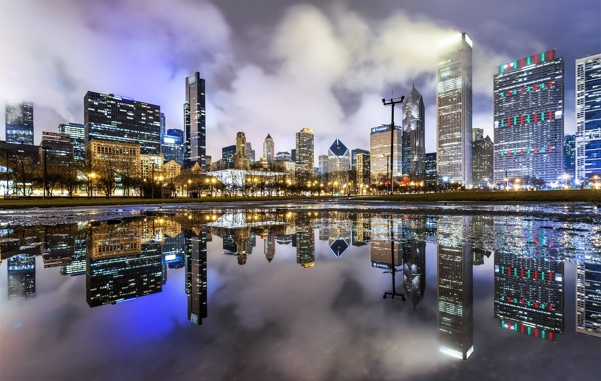 View 桌布 壁紙 — 令人驚嘆的夜間城市景觀，摩天大樓在平靜的水坑中倒映，天空多雲。