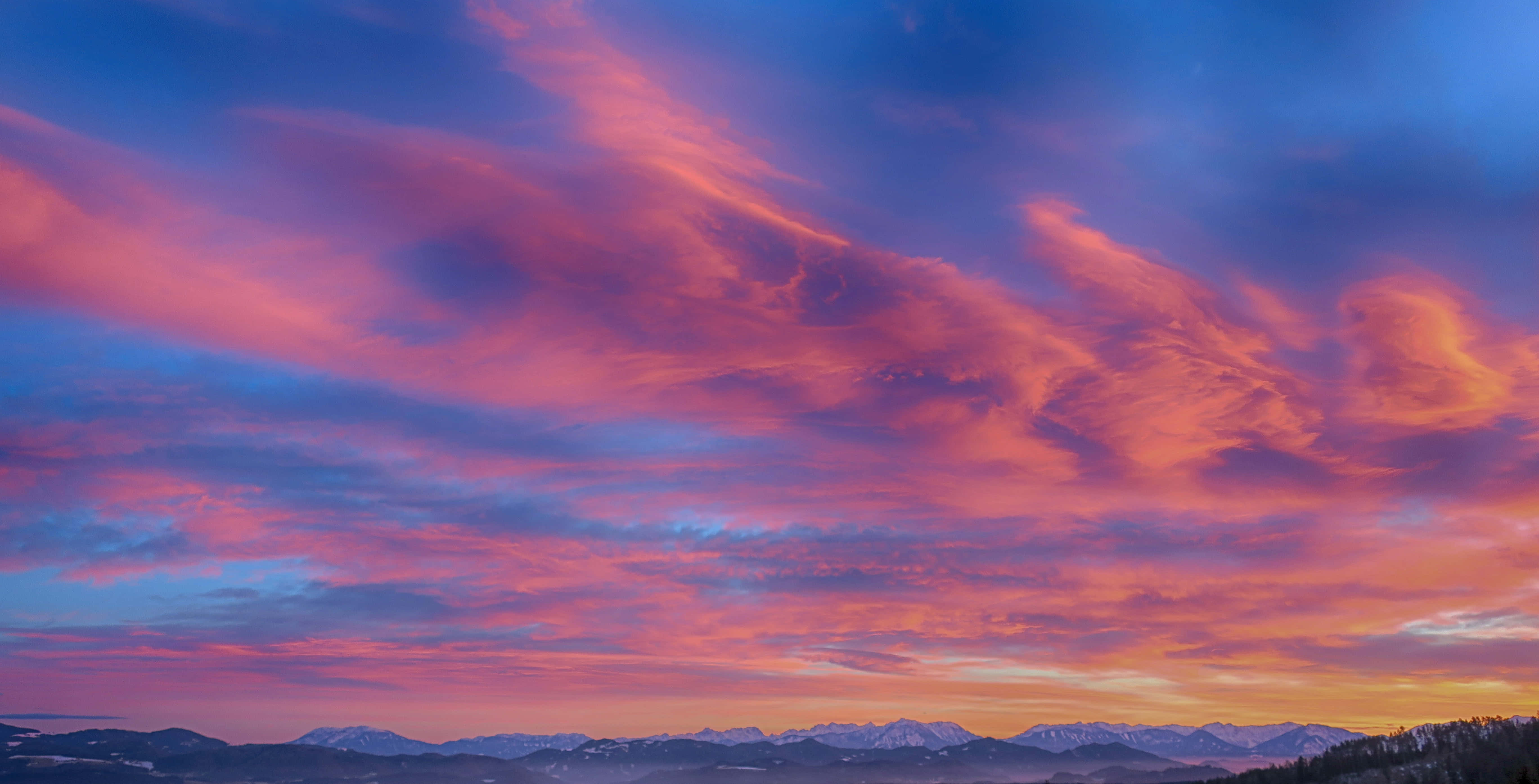 Colorful Sky 桌布 壁紙 — 令人驚嘆的日落將天空染成火熱的粉紅色和橙色，映照在白雪覆蓋的山峰之上。