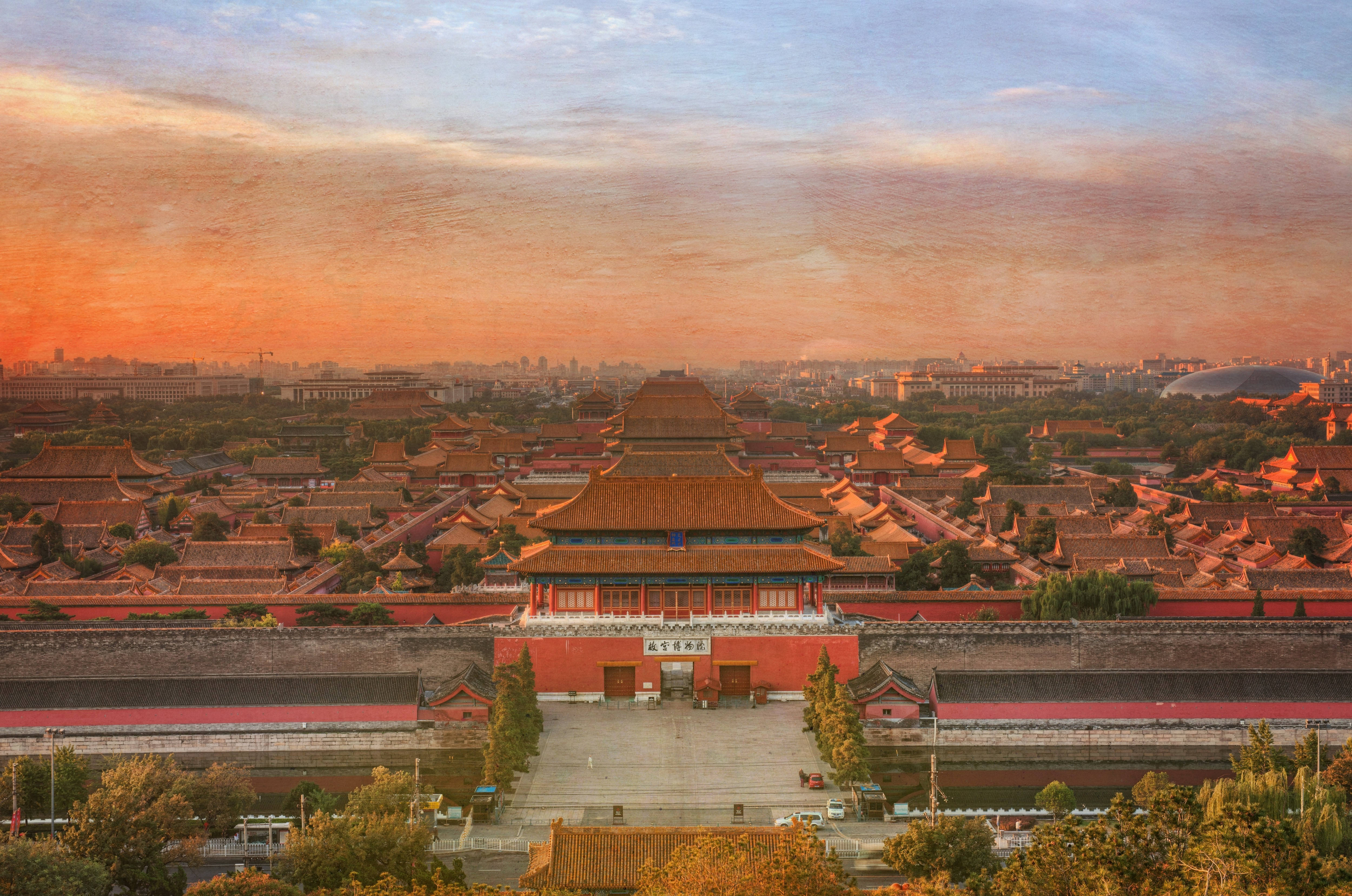 中國 桌布 壁紙 — 令人驚嘆的日落將故宮沐浴在溫暖的橙色光芒中，傳統屋頂和紅牆延伸在歷史悠久的城市景觀中。