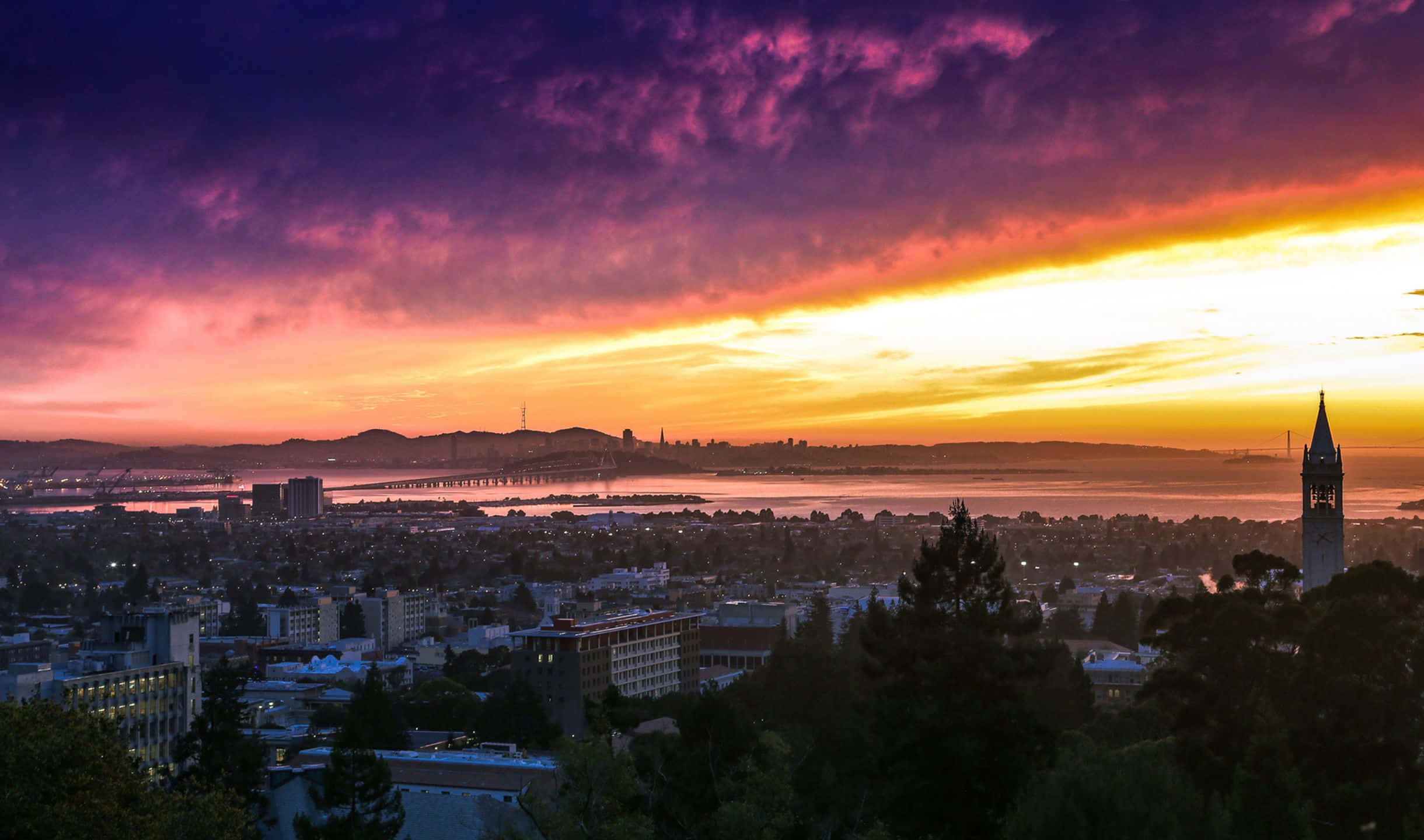 2440x1440 San Francisco 桌布 壁紙 — 令人驚嘆的日落將舊金山的天際線染成火熱的橙色和深紫色，遠處的金門大橋閃閃發光。
